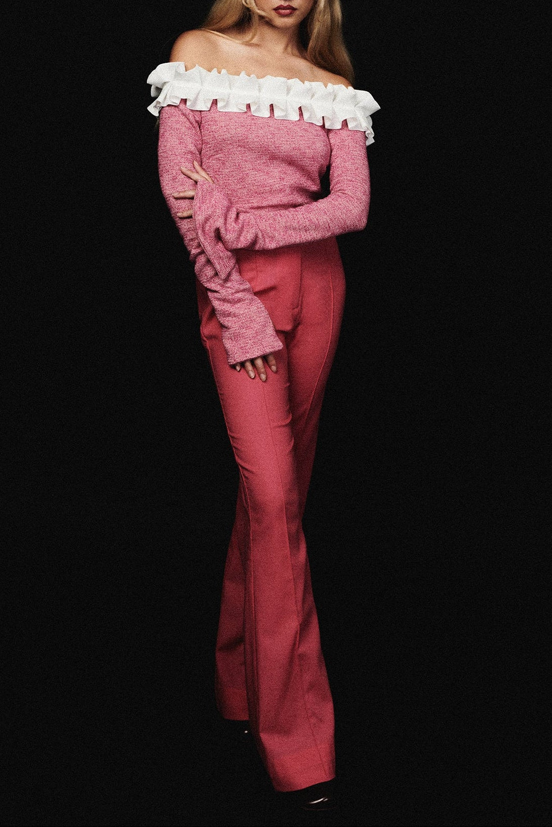 Woman in high waisted pink pant with flared leg and pin tuck detail. Styled with pink off shoulder shirt.