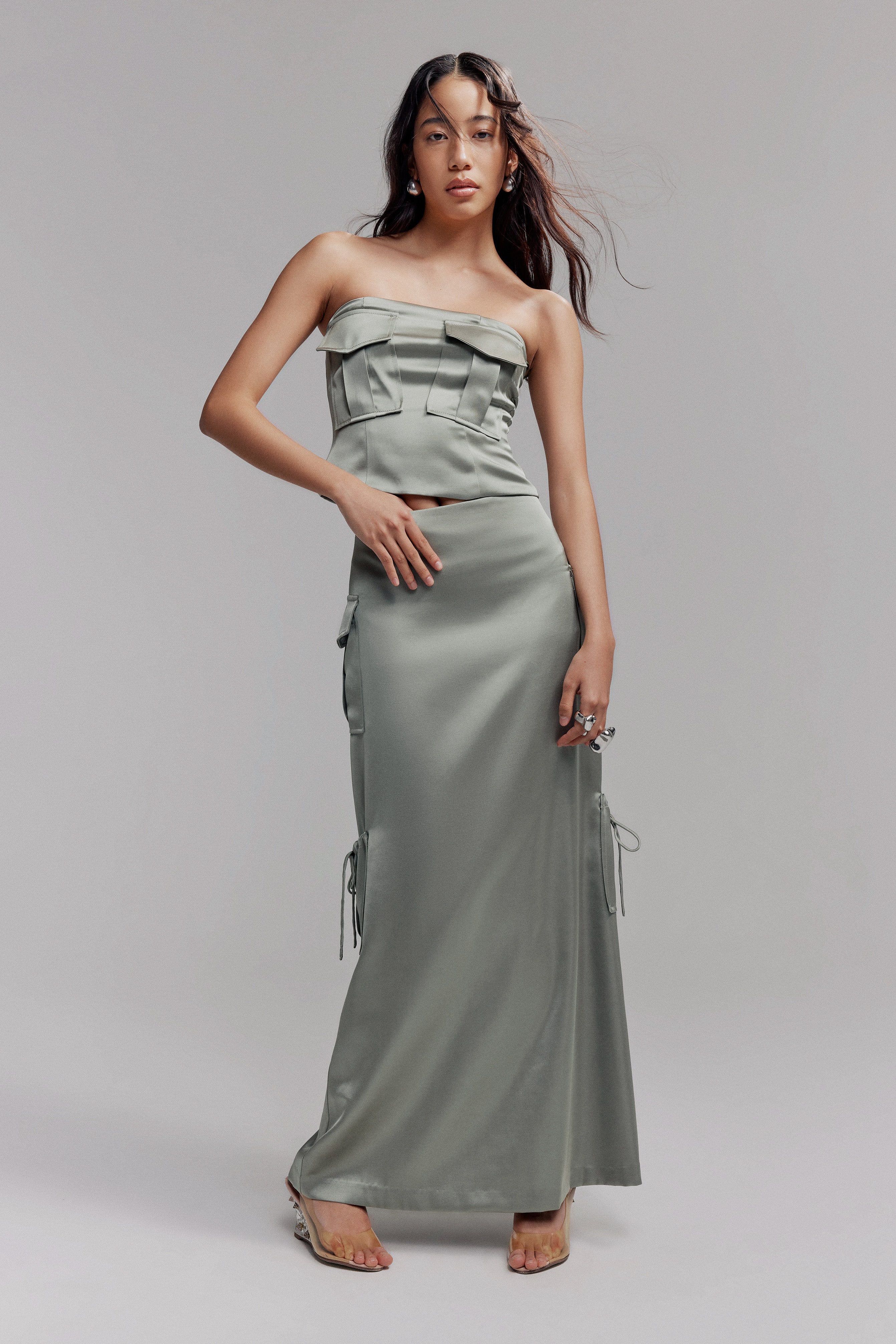 Woman in sage satin maxi skirt featuring cargo pockets. Styled with matching sleeveless crop top with two cargo pockets on the bust.