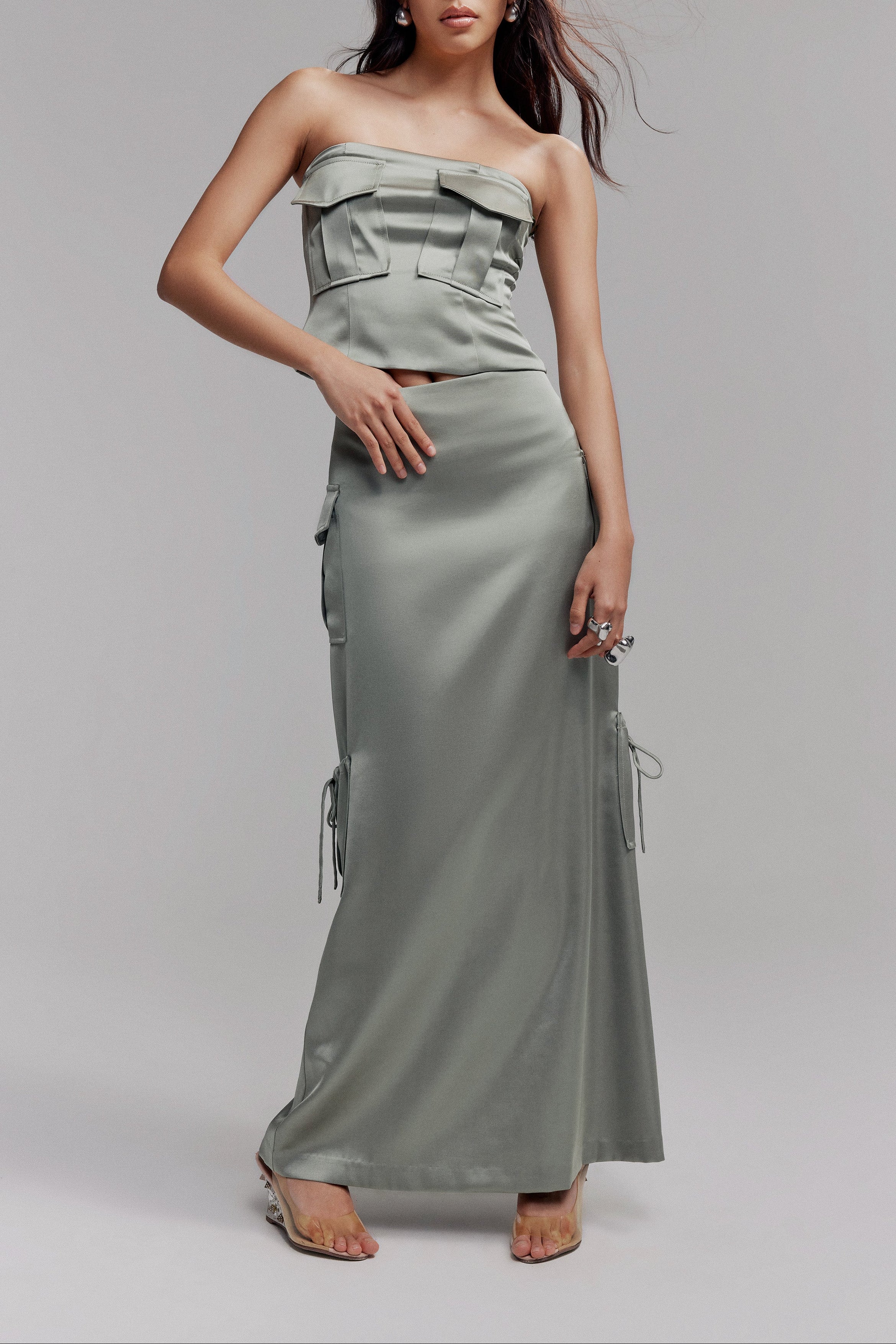 Woman in sage satin maxi skirt featuring cargo pockets. Styled with matching sleeveless crop top with two cargo pockets on the bust.