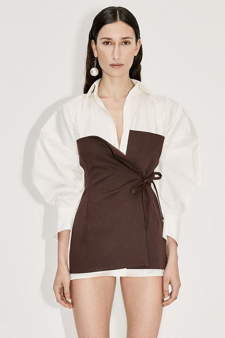 Woman in white mini shirt dress with voluminous sleeves and brown layered front asymmetric tie detail.