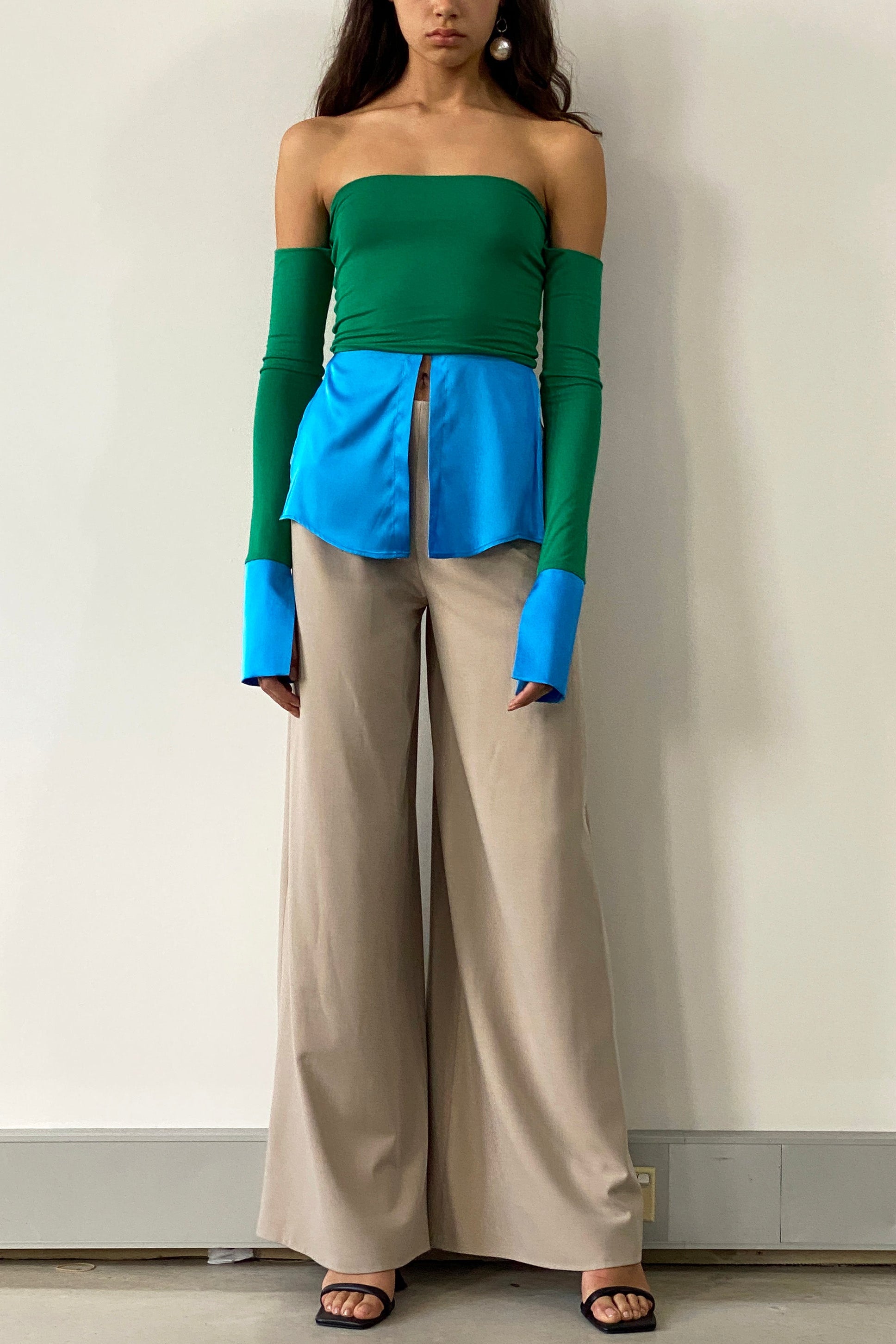 Woman in green off shoulder long sleeve crop top with blue hem and collars inspired by traditional shirting. Styled with beige trousers.