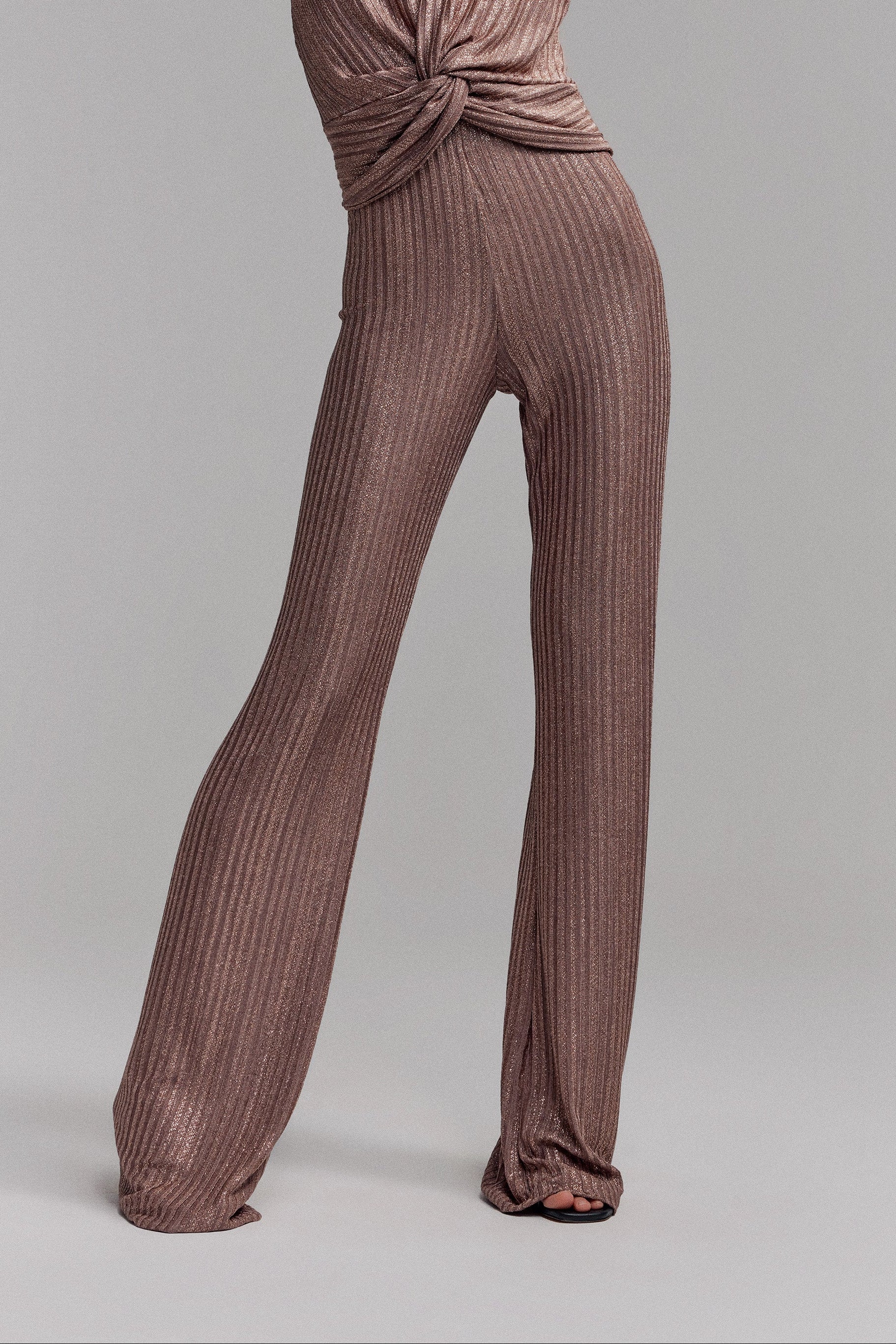 Woman in long rib knit bronze pants. High waisted and slightly wide leg. Sparkly fabrication perfect for party's. Styled with matching halter neck top.