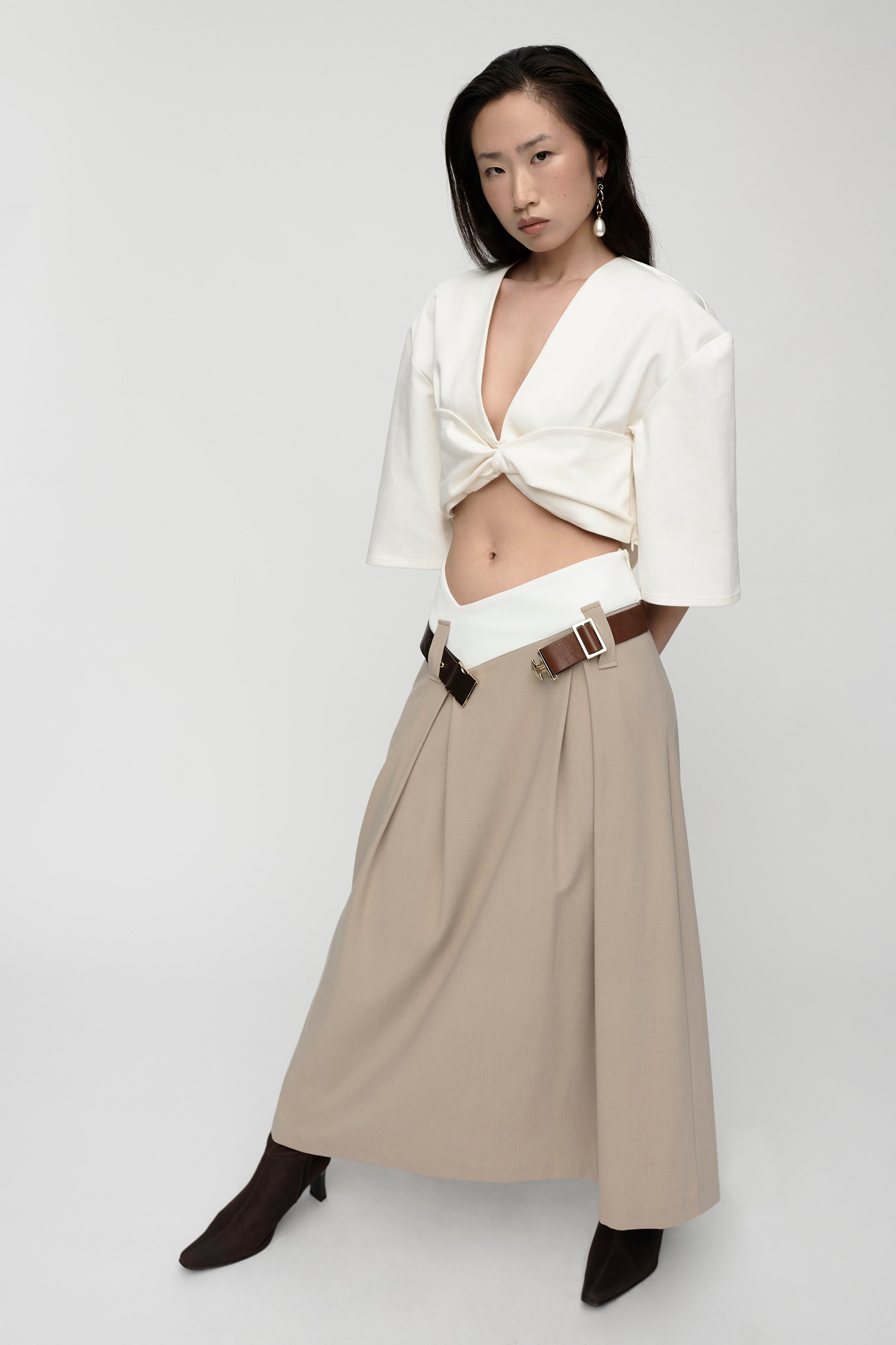 Woman in mid length sleeve, v-neck, cropped white top. Styled with long beige skirt and boots.