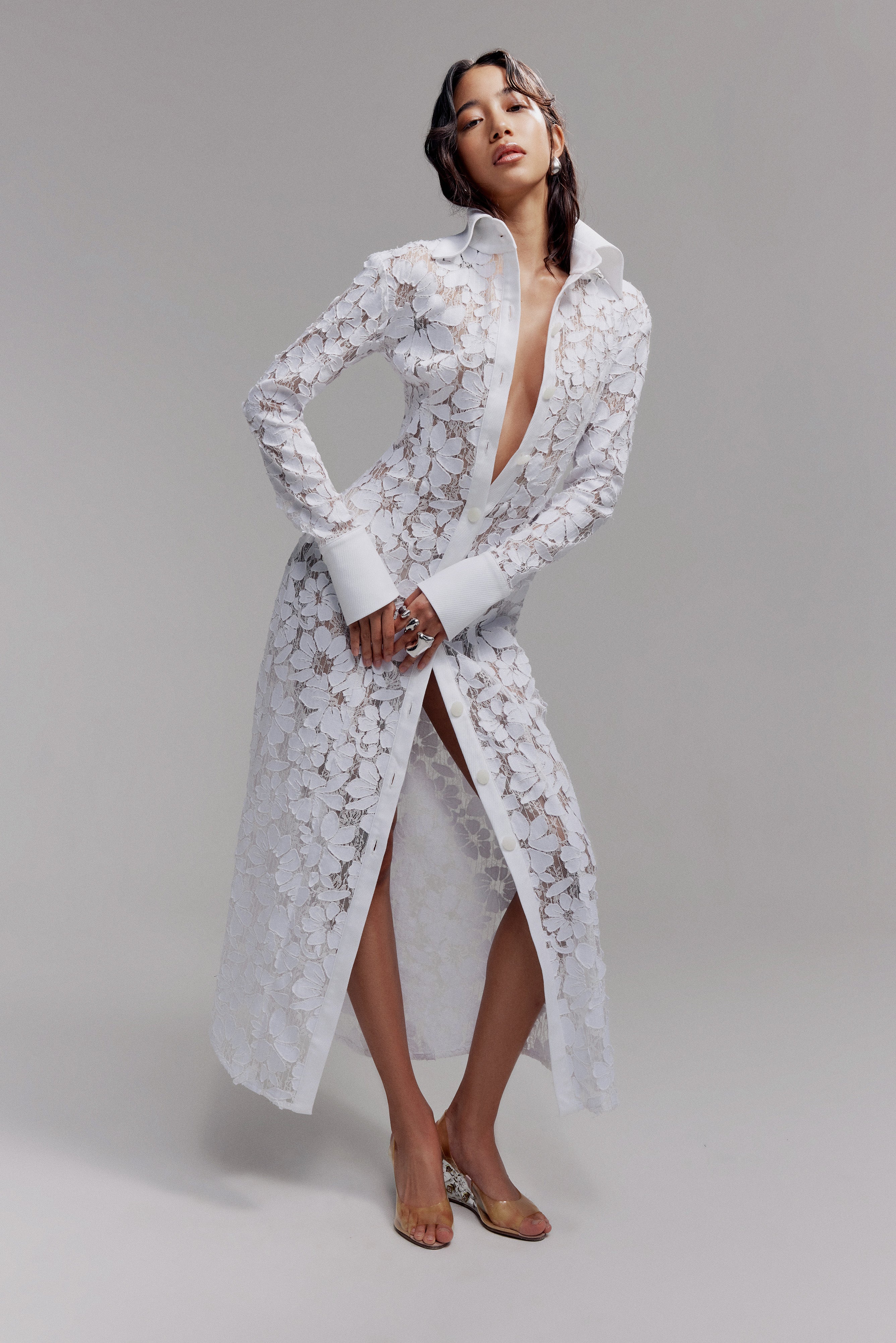 Woman in maxi white lace shirt dress with long sleeves, exaggerated collar and button front closure.