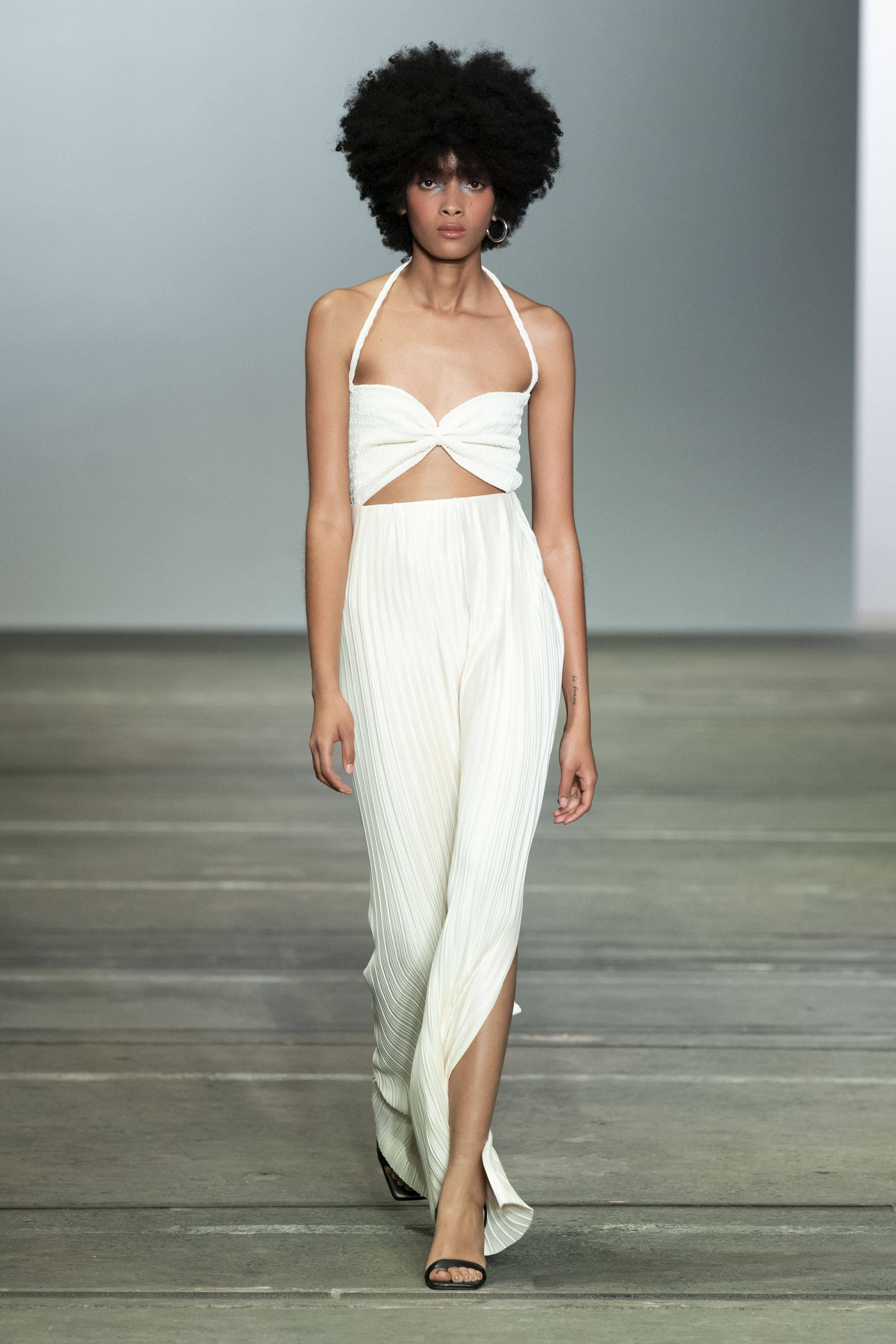 Woman in white halter neck maxi dress. Featuring side slits and soft pleating in the skirt and cut out and cinched bust detail on the top. Perfect for vacation.