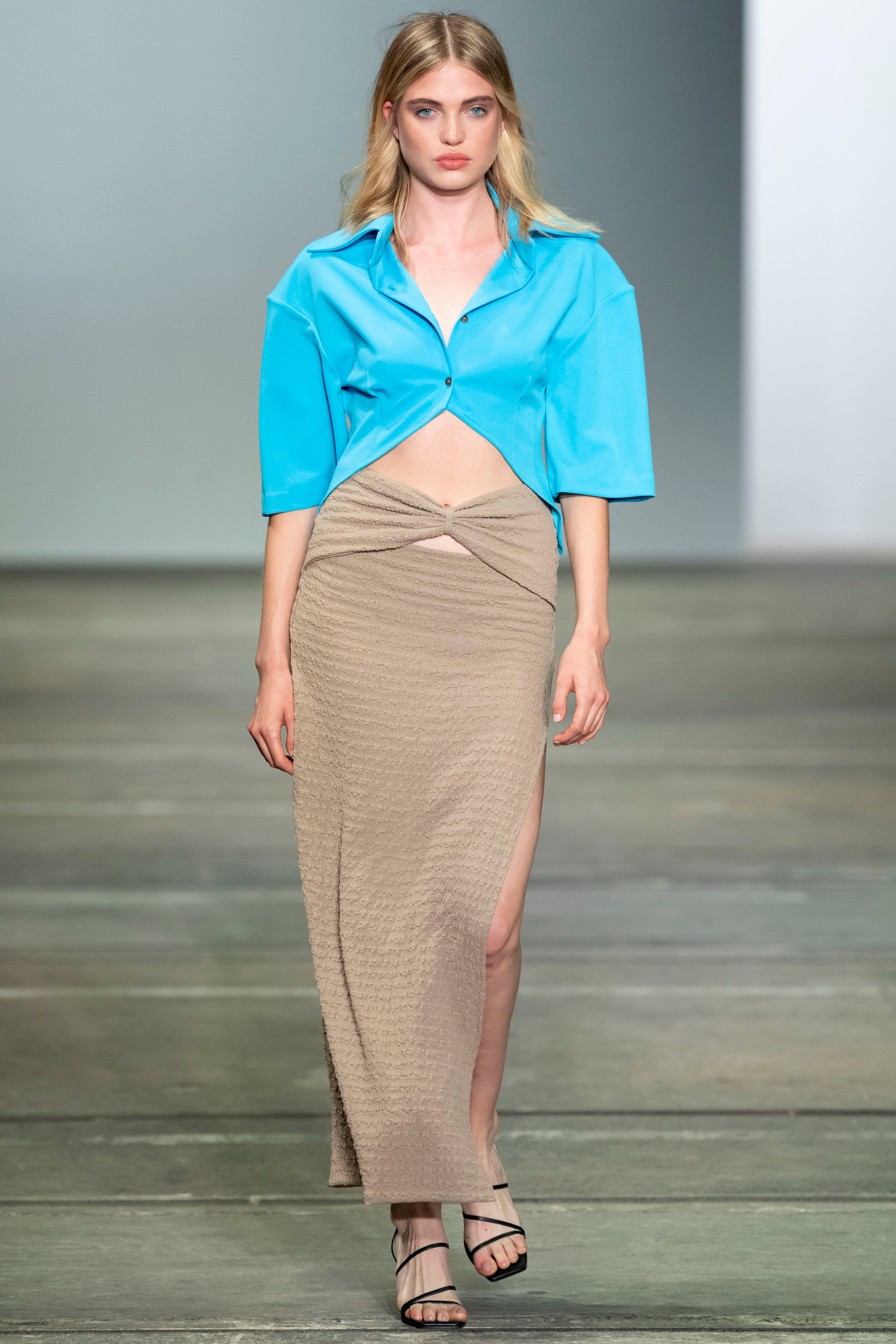 Woman in blue button down shirt with cornered hem, large collar and boxy sleeves. Styled with maxi beige skirt.