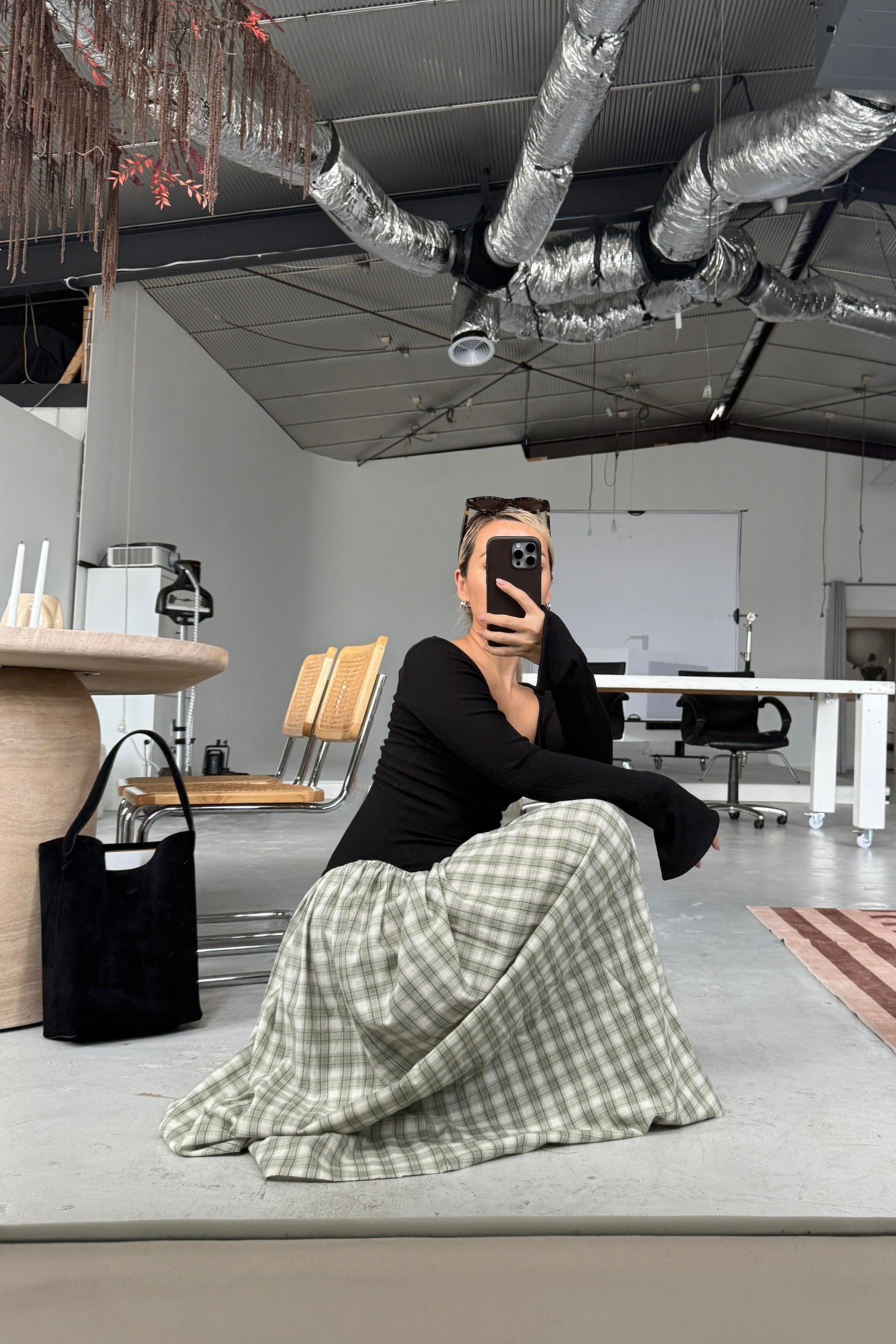 Woman in long sleeve black dress, with extra long sleeves, scooped neckline, and artfully gathered green plaid skirt. Top flatters the figure whilst the skirt flows with every movement. Can be dressed up or down.