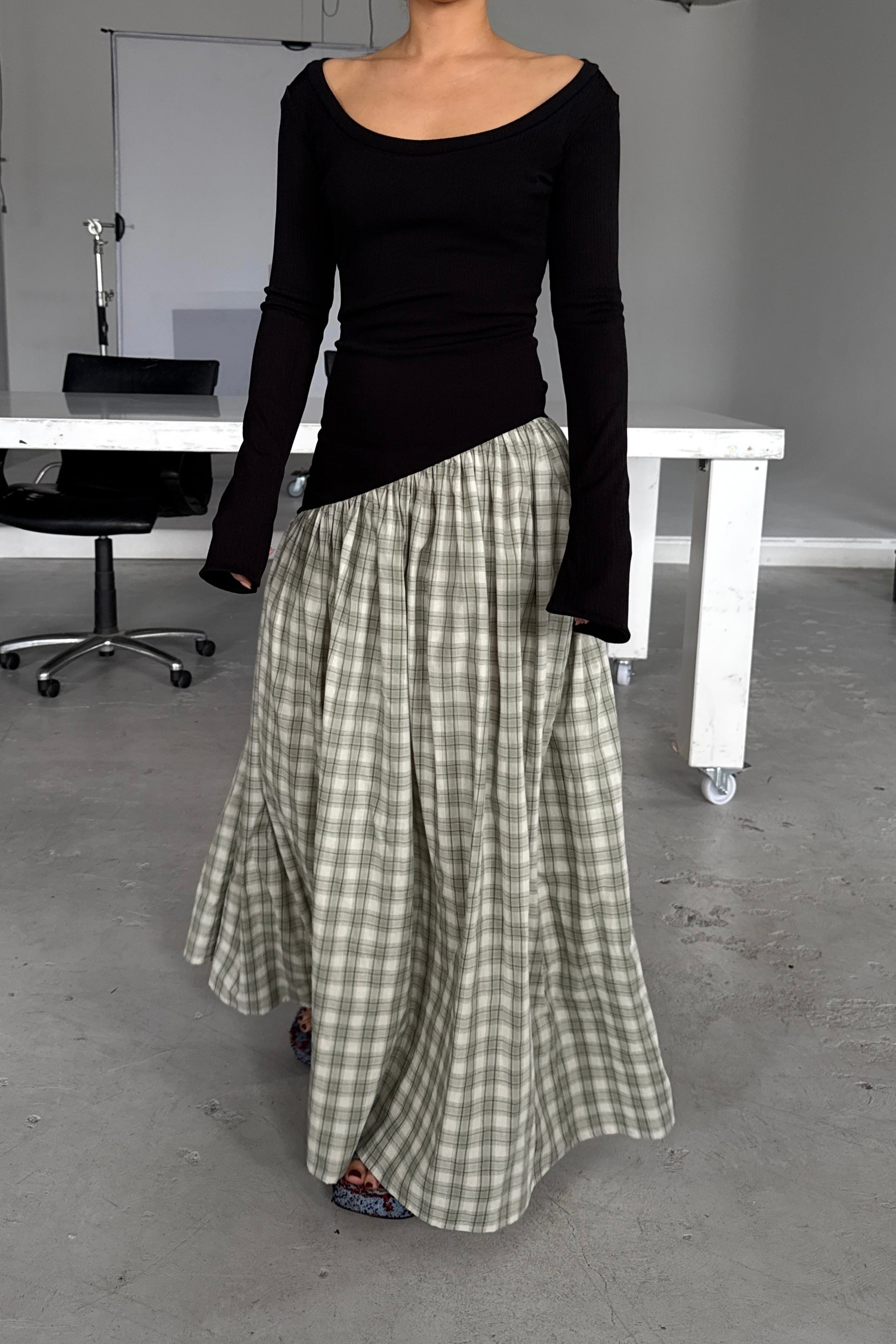 Woman in long sleeve black dress, with extra long sleeves, scooped neckline, and artfully gathered green plaid skirt. Top flatters the figure whilst the skirt flows with every movement. Can be dressed up or down.