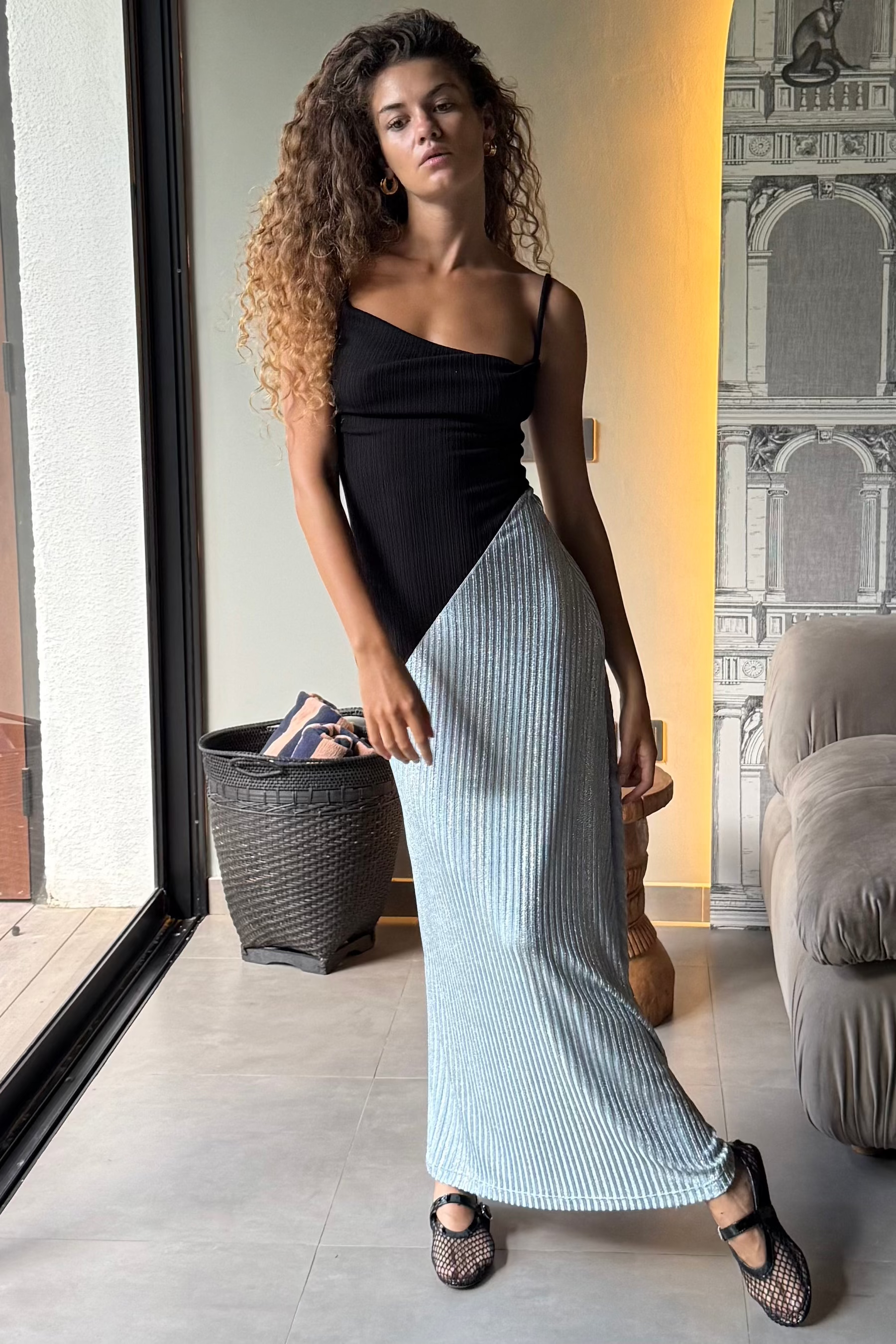 Woman in a long black dress with cowl neck and asymmetric sparkly blue skirt. Spaghetti straps and maxi length. Summer soirée essential.