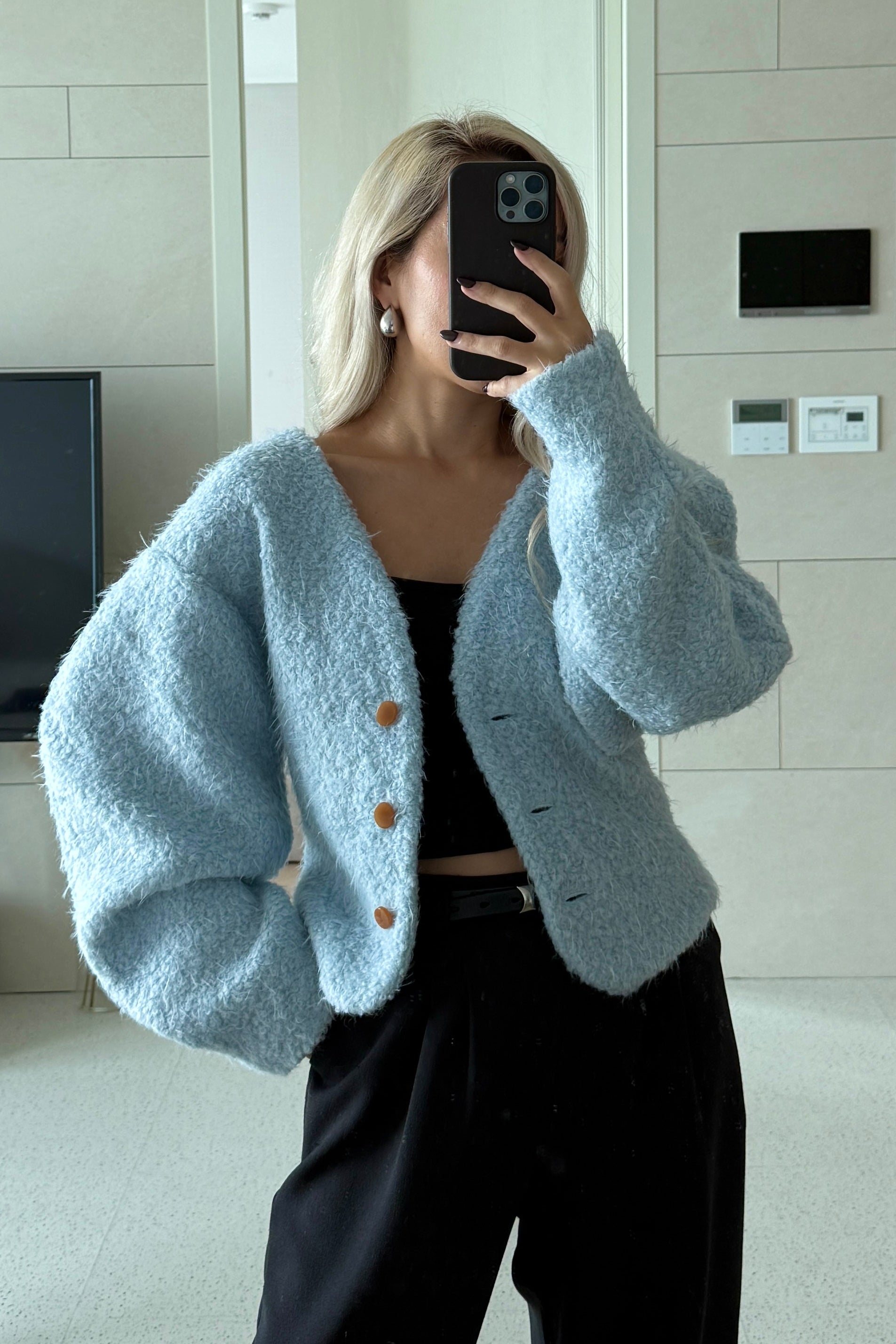 Woman in baby blue fuzzy volume sleeve cardigan. Paired with a black tank top and trousers. Officewear essential.