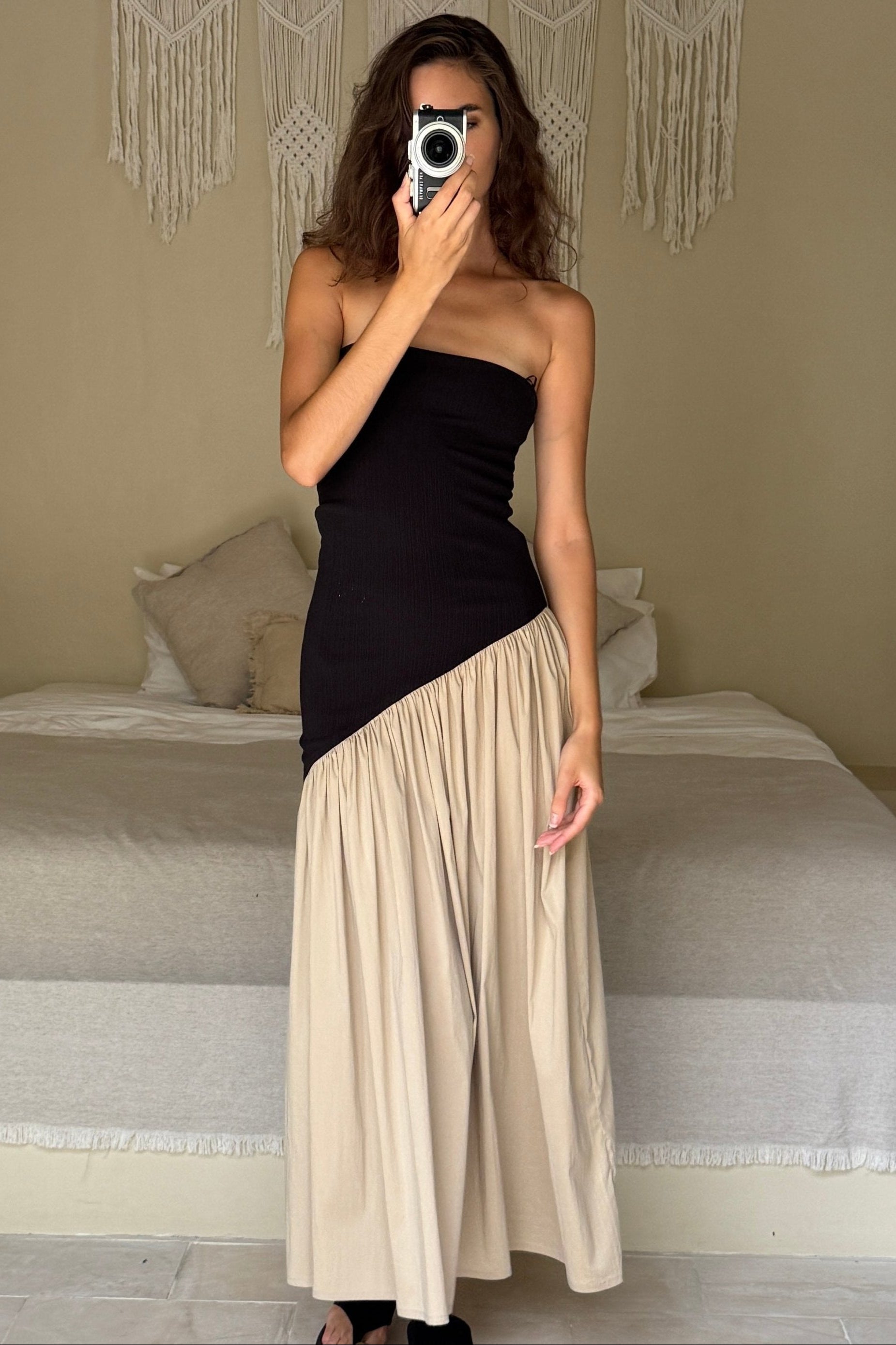 Woman in strapless black maxi dress with asymmetric artfully gathered beige skirt. Top flatters the figure and skirt adds flow with every movement. Perfect for beach outings and summer soirées.