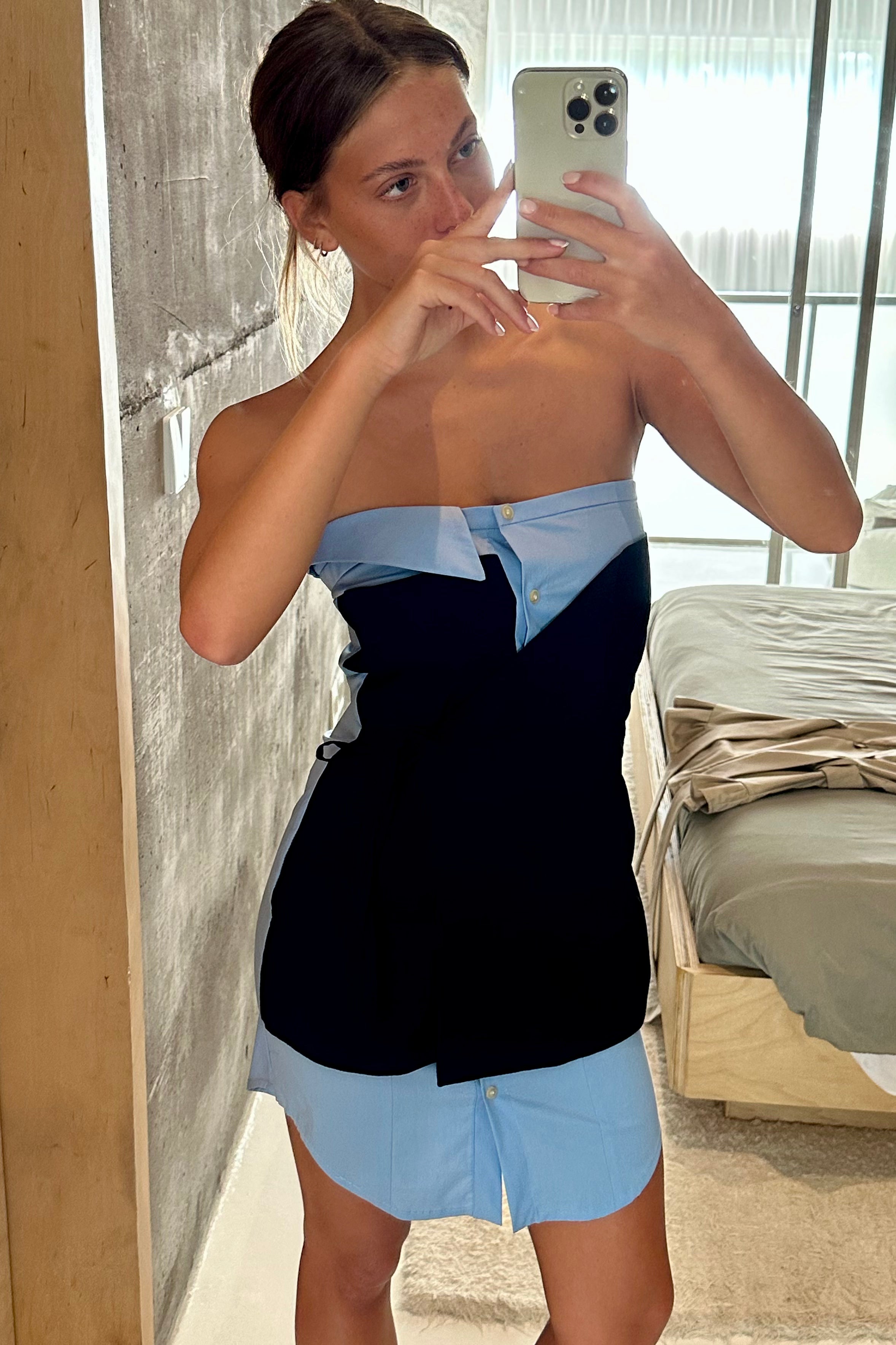 Woman in baby blue strapless mini dress with elements of traditional shirting. Layered black asymmetric tie front detail.