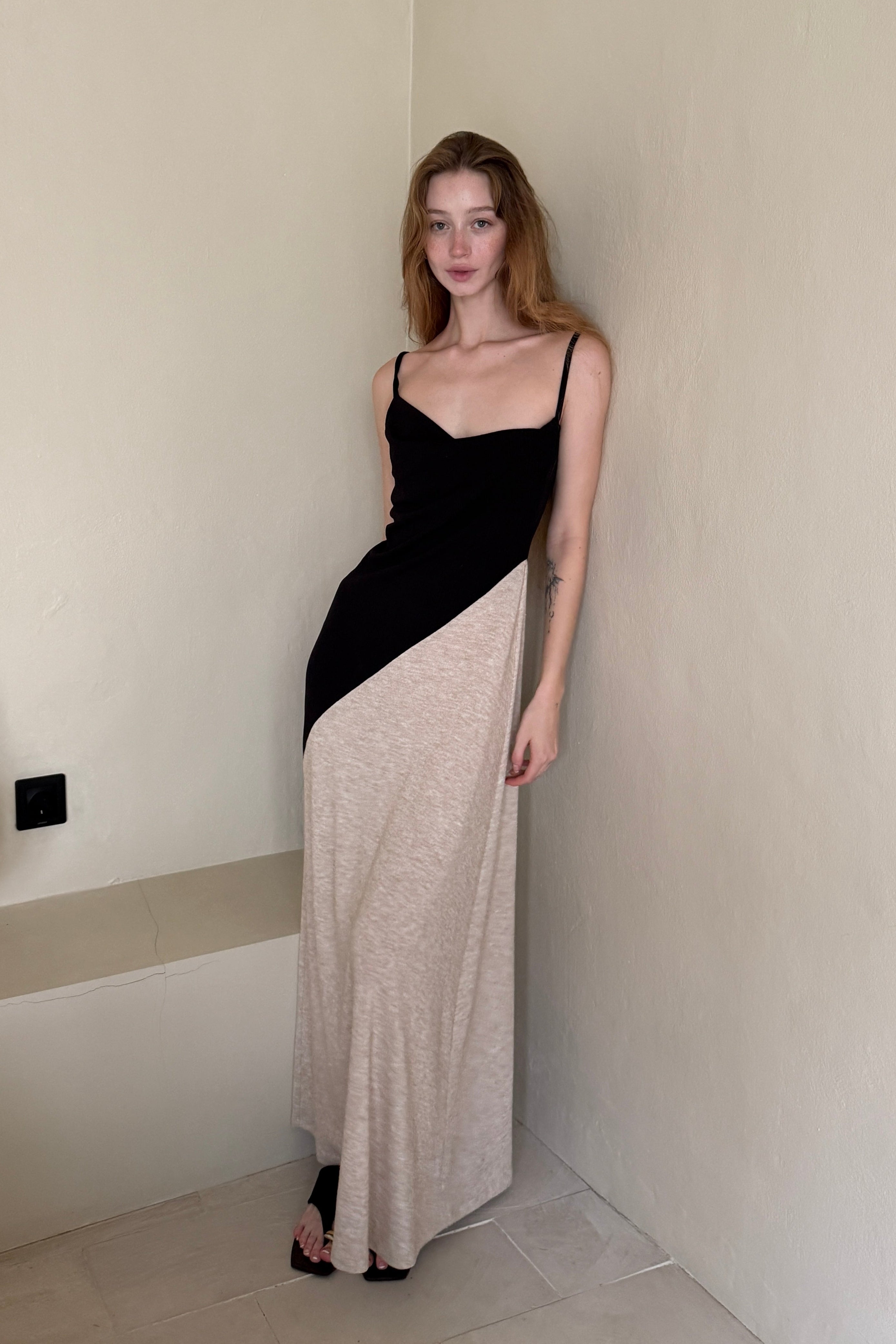 Woman in a long black dress with cowl neck and asymmetric beige skirt. Spaghetti straps and maxi length. Summer soirée essential.