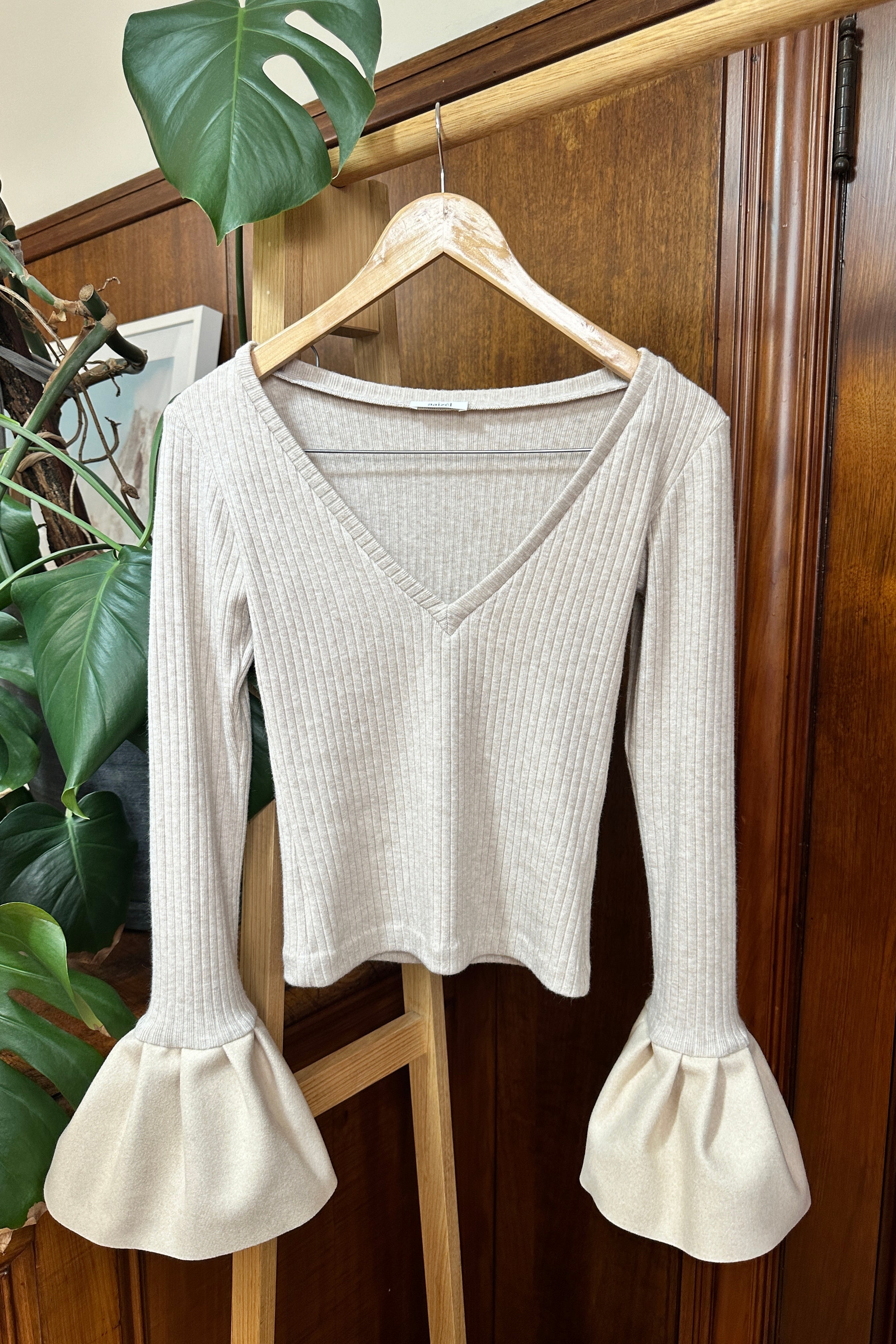 Beige soft rib knit top with v-neck, long sleeves, and flared cuff details.