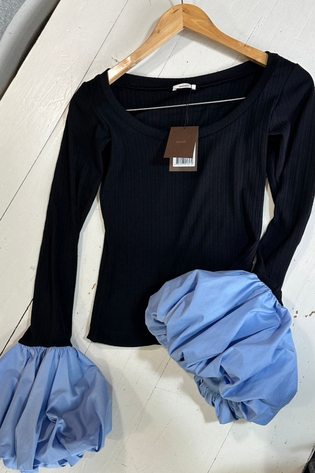 Flat lay of black long sleeve rib knit top with round neckline and blue balloon details on cuffs.