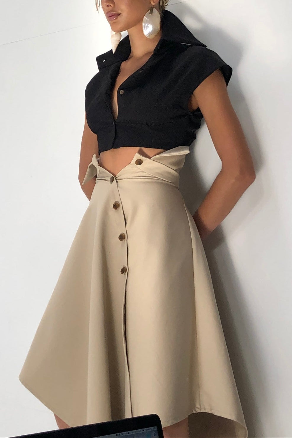Woman in black cropped sleeveless button up shirt. Styled with beige skirt.