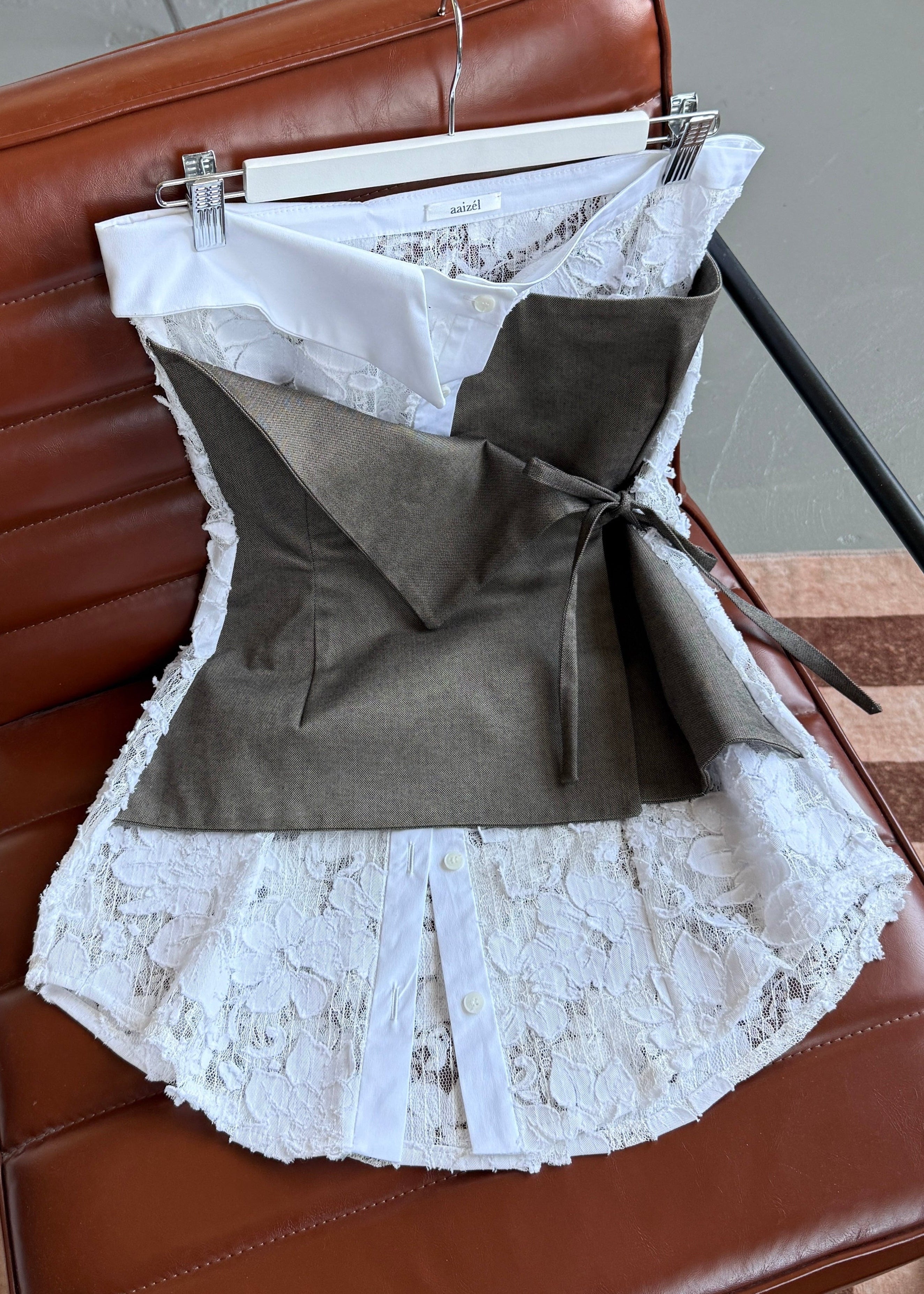 Flat lay of white lace strapless top with elements of traditional shirting. Layered beige asymmetric tie front detail.