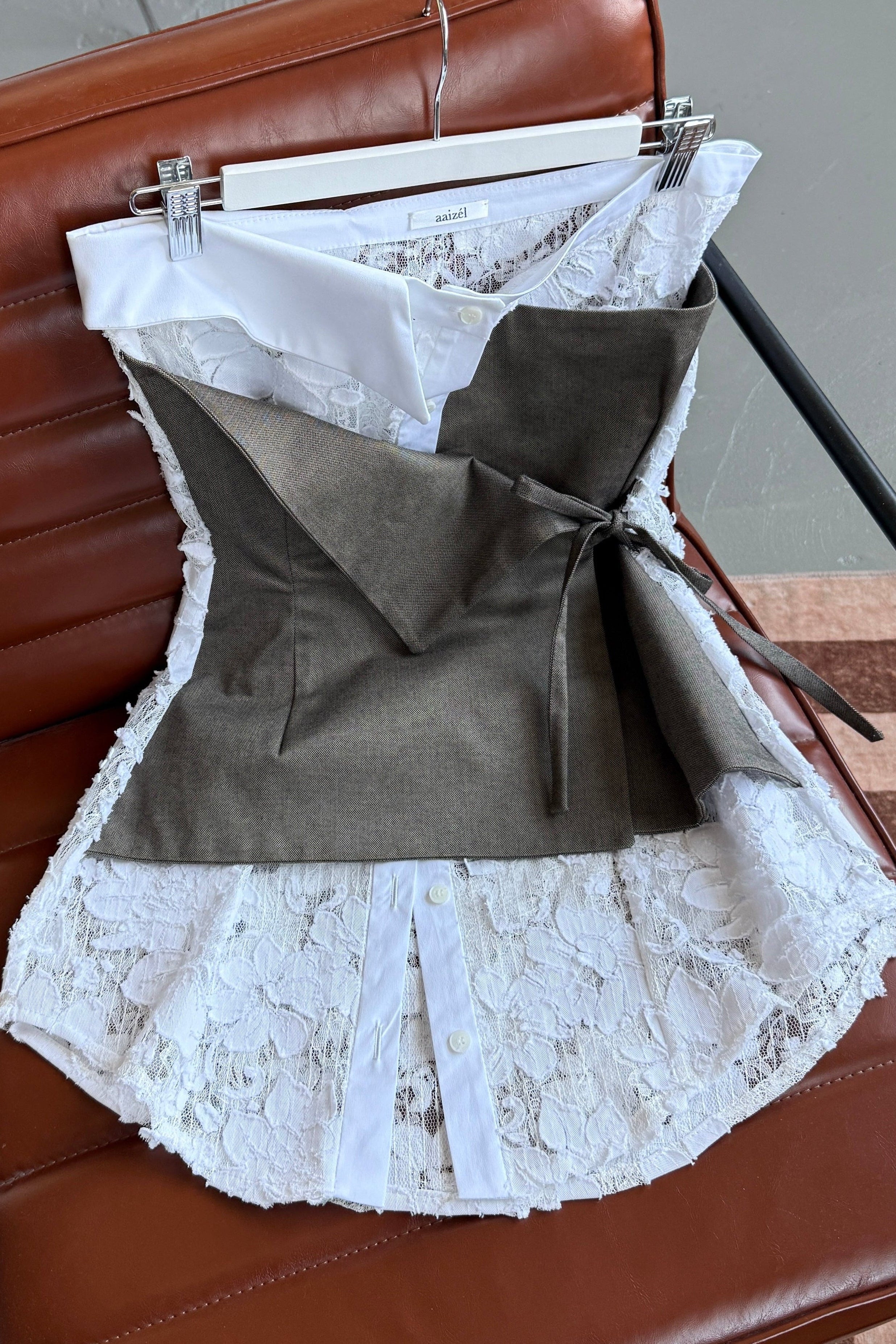 Flat lay of white lace strapless top with elements of traditional shirting. Layered beige asymmetric tie front detail.