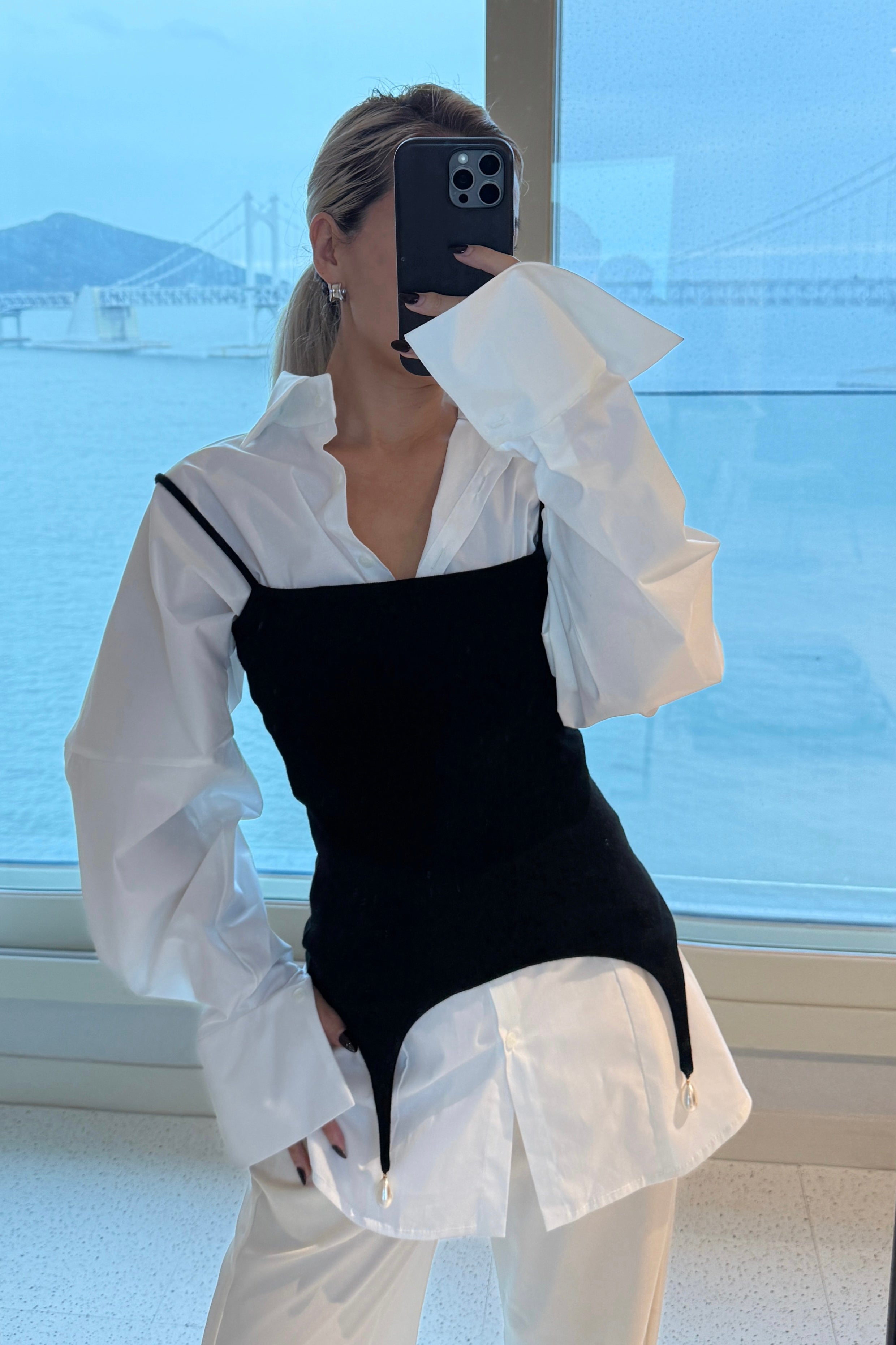 White volume sleeve shirt dress with form fitting black tank with pearl hem detail on top. Styled over cream pants.