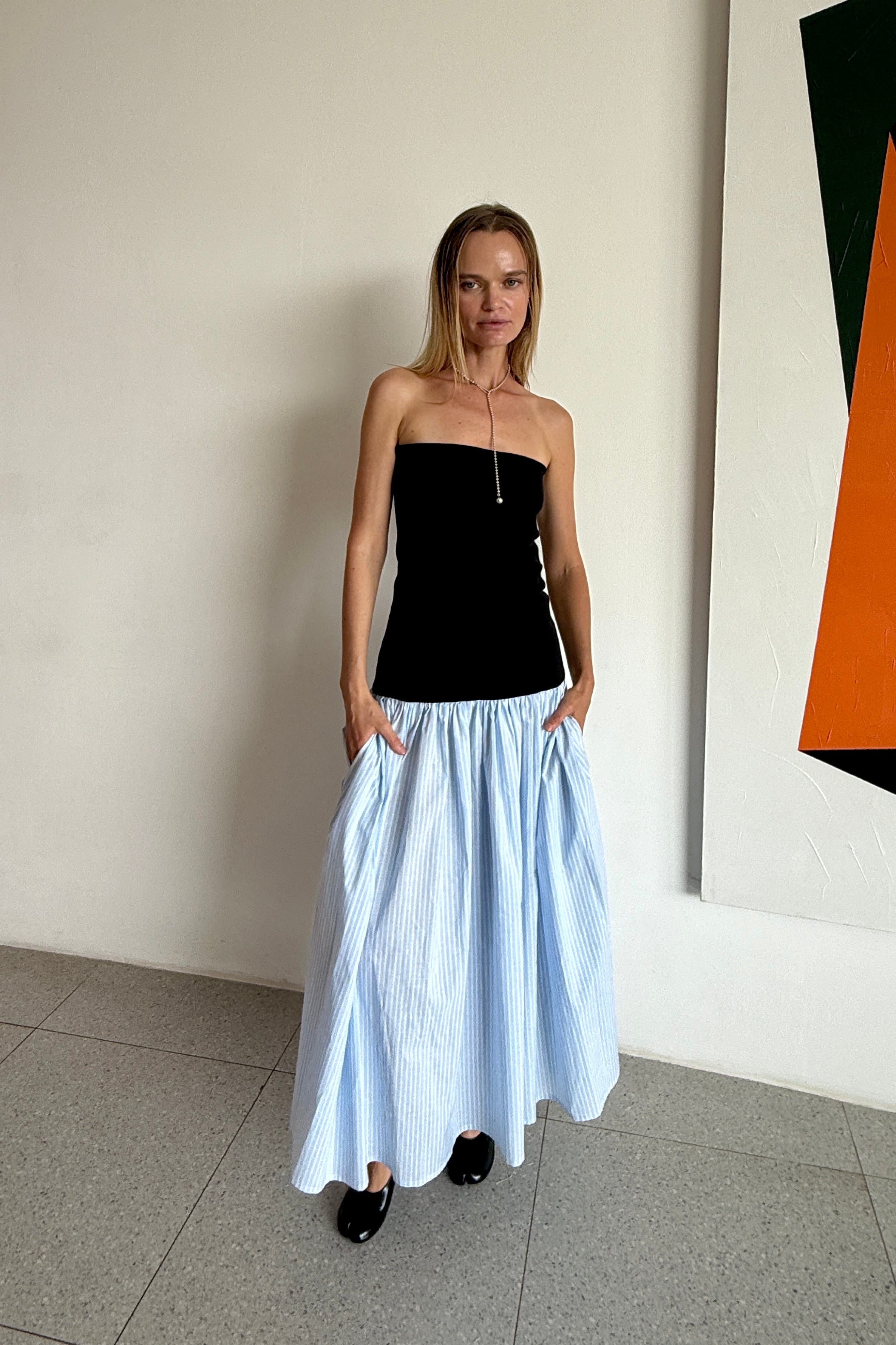 Woman wearing a black strapless dress with light blue striped gathered skirt.