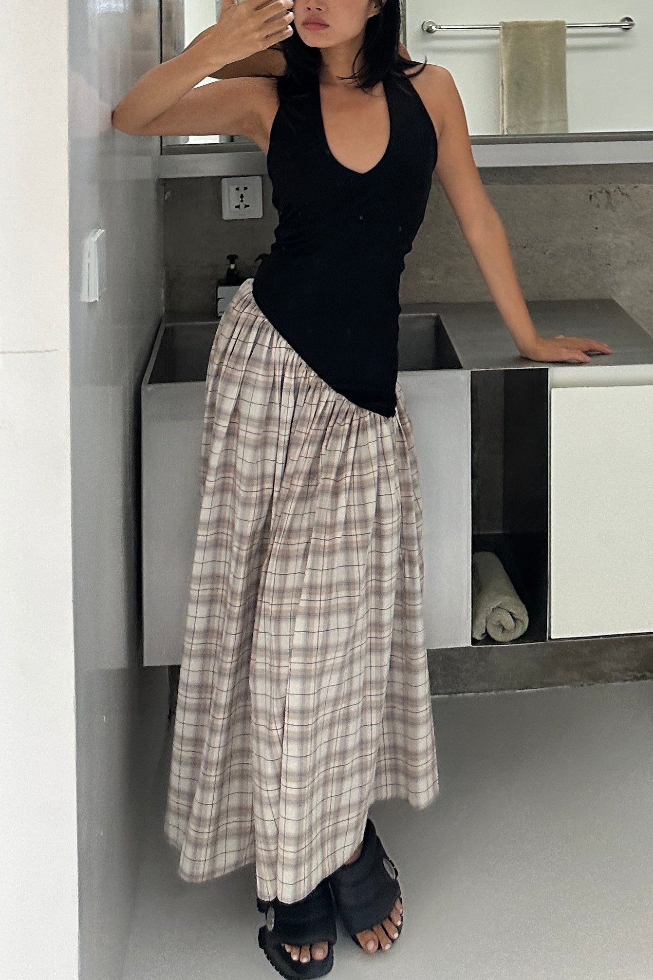 Woman in a black halter maxi dress with v-neck line and asymmetric artfully gathered plaid skirt. Top flatters the figure and skirt adds flow with every movement. Perfect for beach outings and summer soirées.