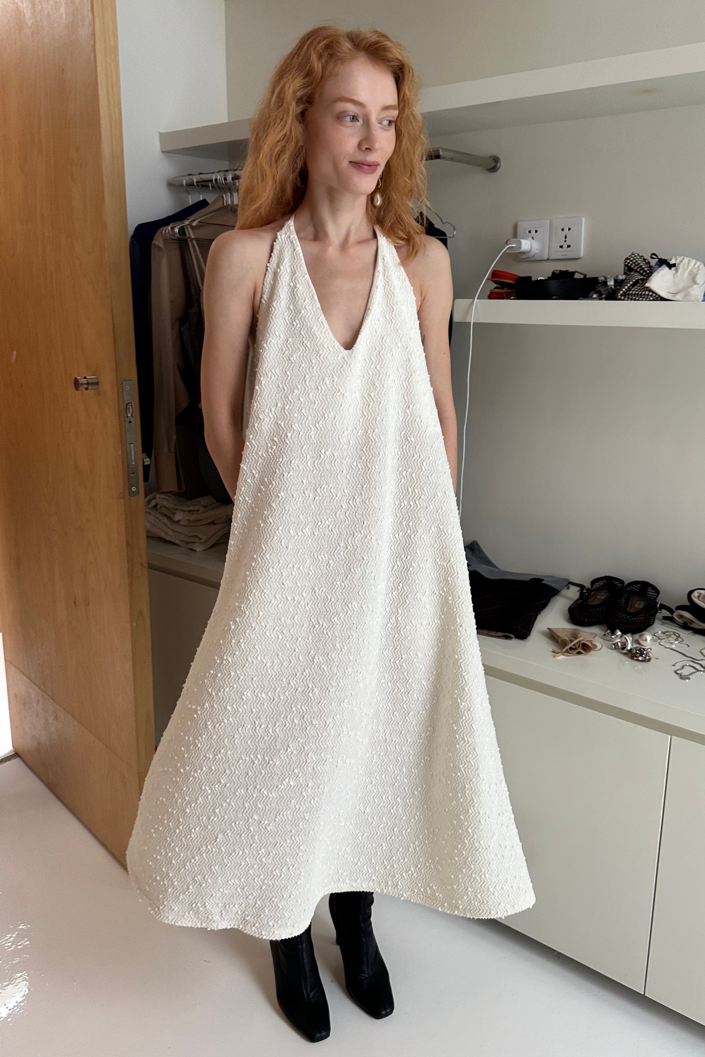 Woman in a white a-line shapeless draped dress with a scooped v-neck, featuring subtle textural details and fine sequins. Perfect for beach days or Summer outings.