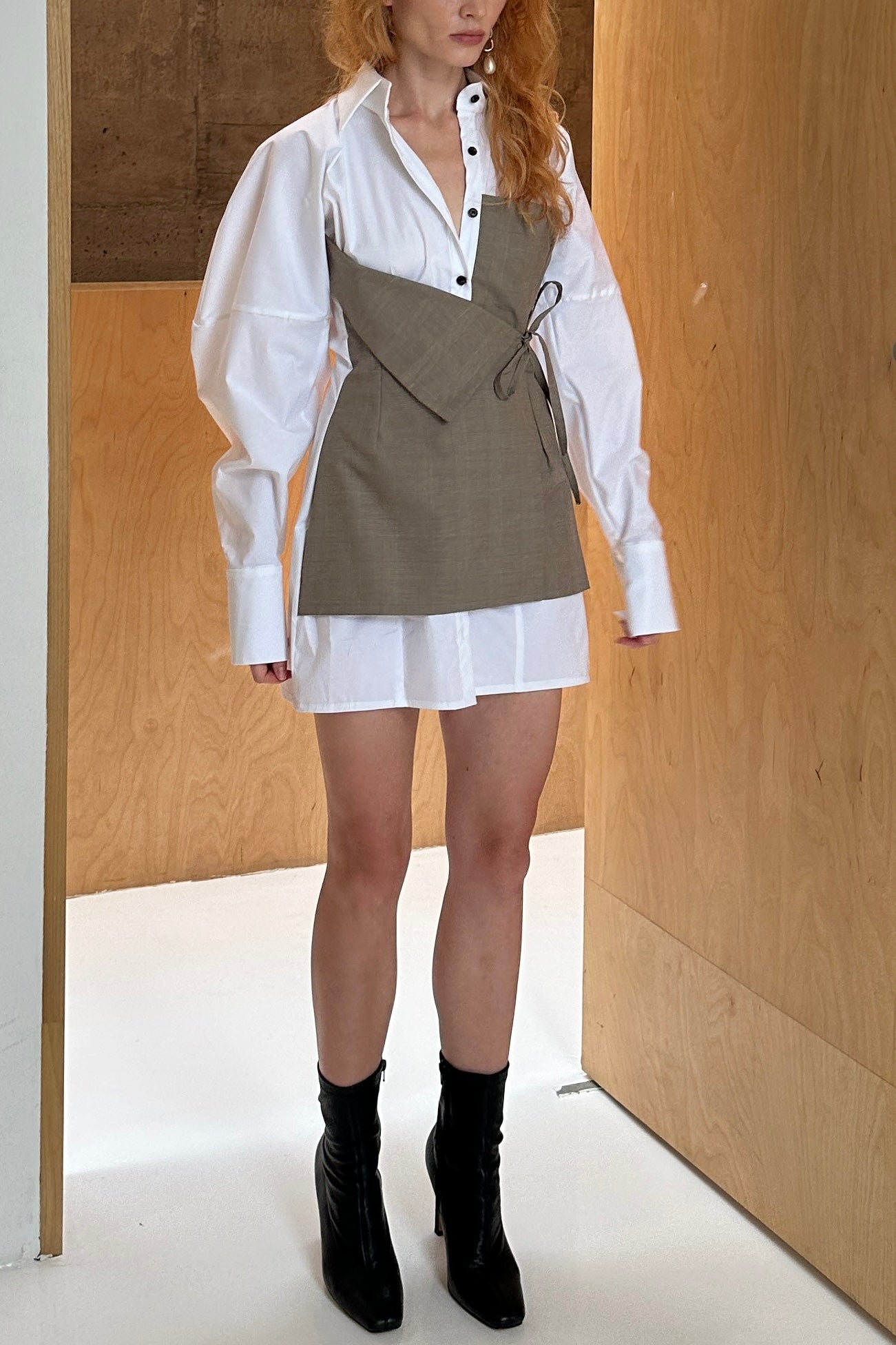 Woman in white shirt dress with voluminous sleeve with layered front asymmetric tie detail.