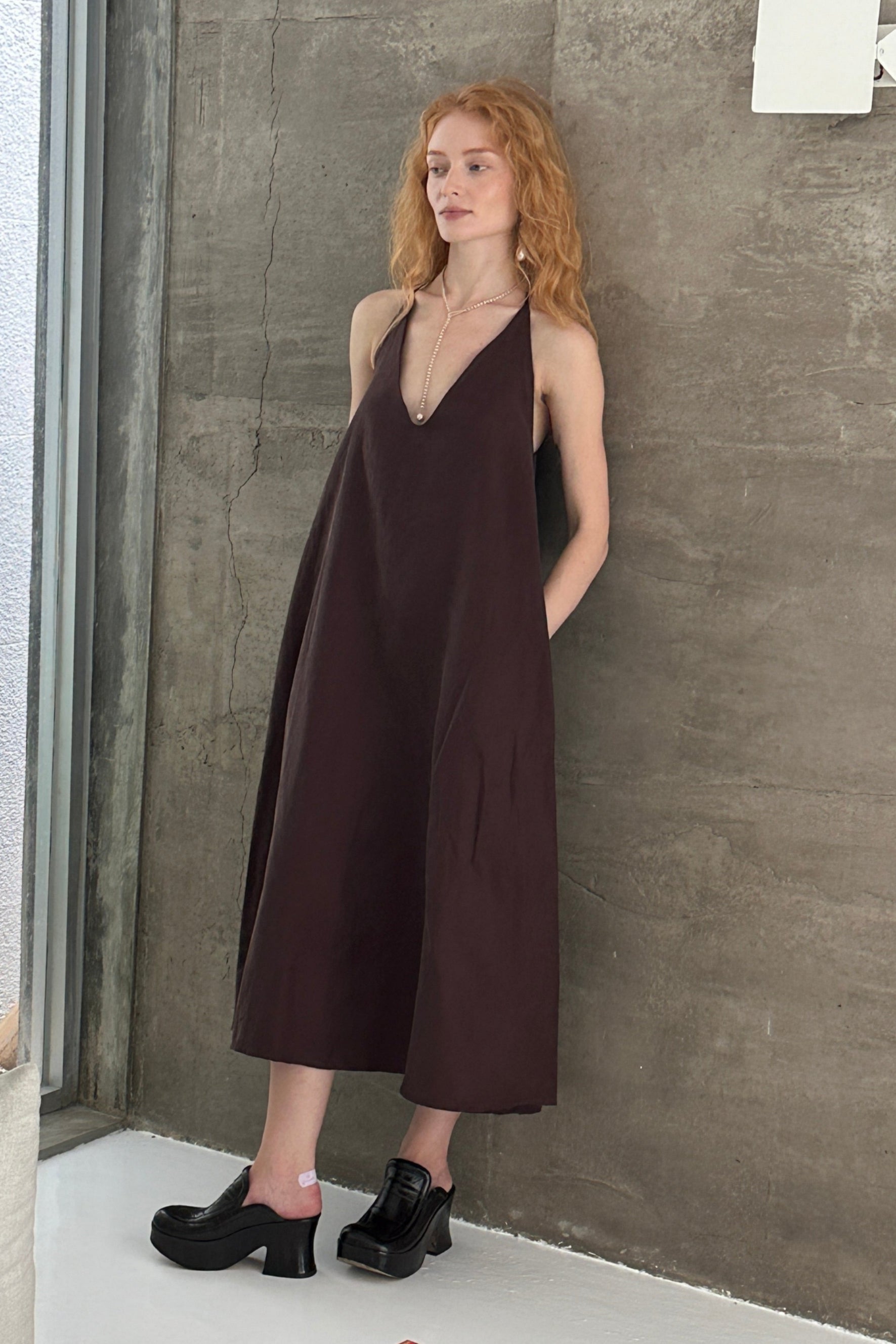 Woman in a brown a-line shapeless draped dress with a scooped v-neck. Styled with gold jewellery. Perfect for beach days or Summer outings.