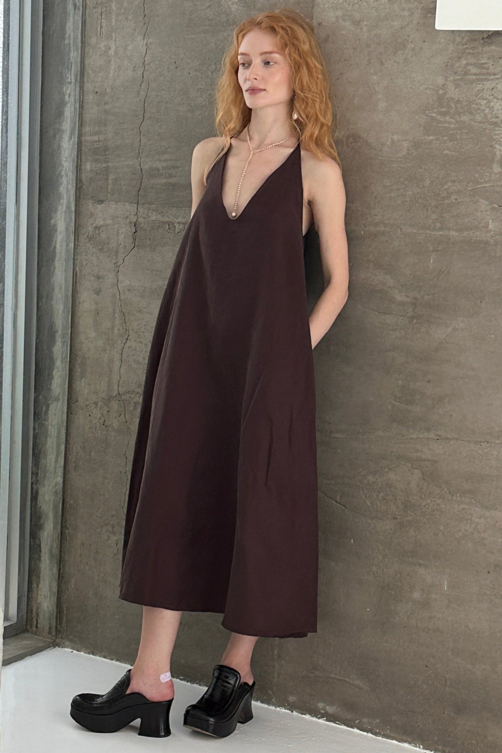 Woman in a brown a-line shapeless draped dress with a scooped v-neck. Styled with gold jewellery. Perfect for beach days or Summer outings.