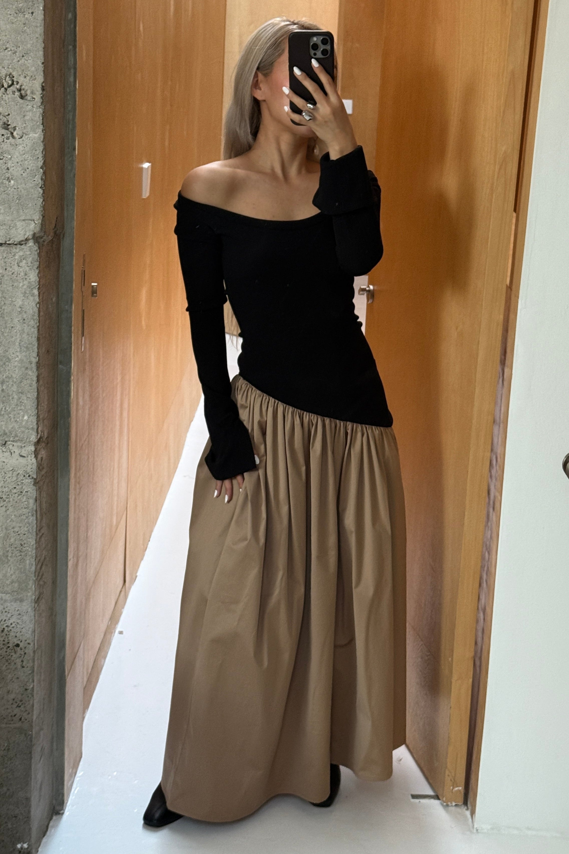 Woman in long sleeve dress, with extra long sleeves, scooped neckline, and artfully gathered asymmetric beige skirt. Styled off the shoulder. Top flatters the figure whilst the skirt flows with every movement. Can be dressed up or down.