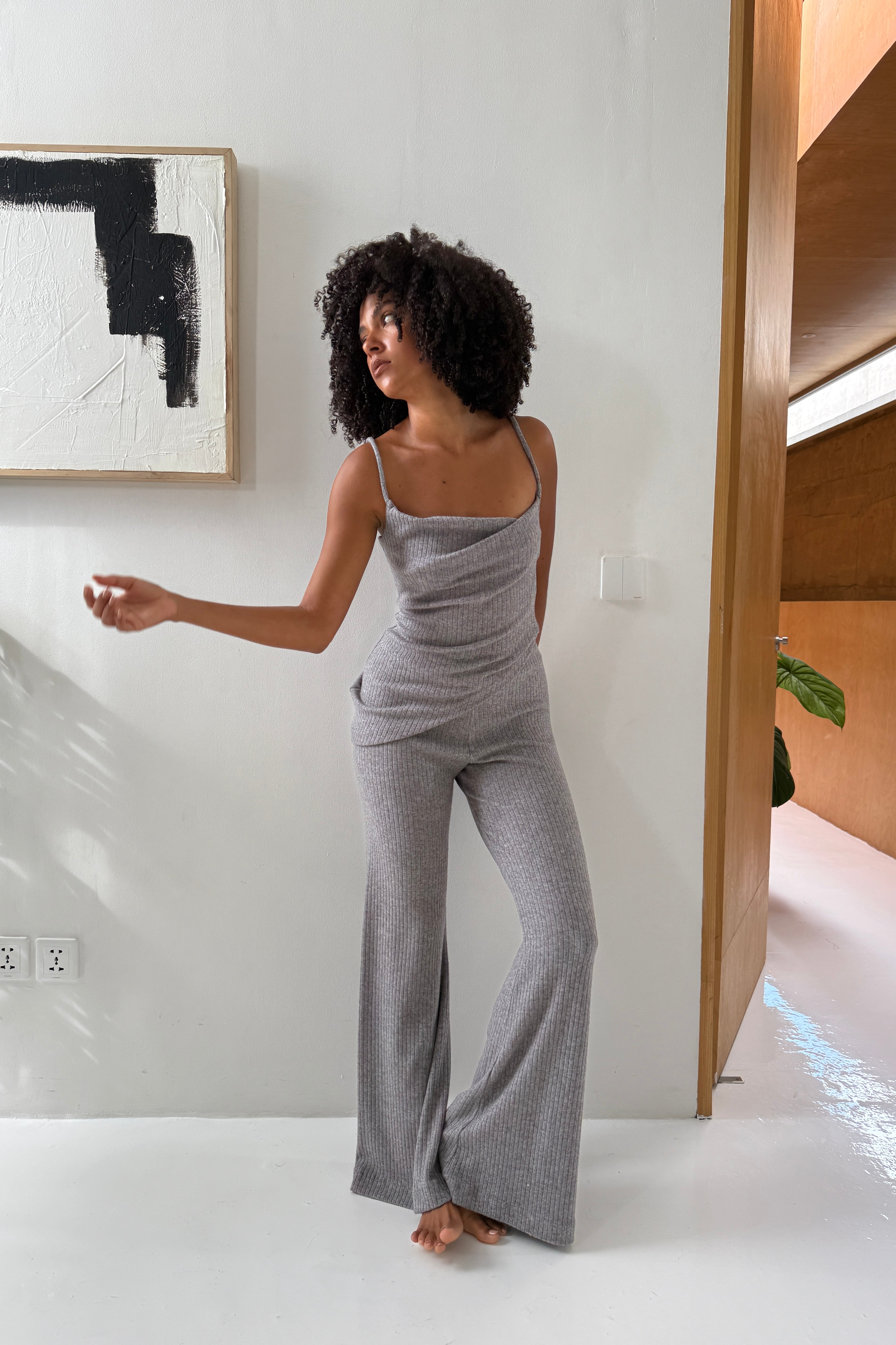 Woman in matching grey loungewear set. Featuring spaghetti strap asymmetric cowl neck top, in soft rib knit, and wide leg pants with elasticised waist. Perfect for running errands and casual outings.