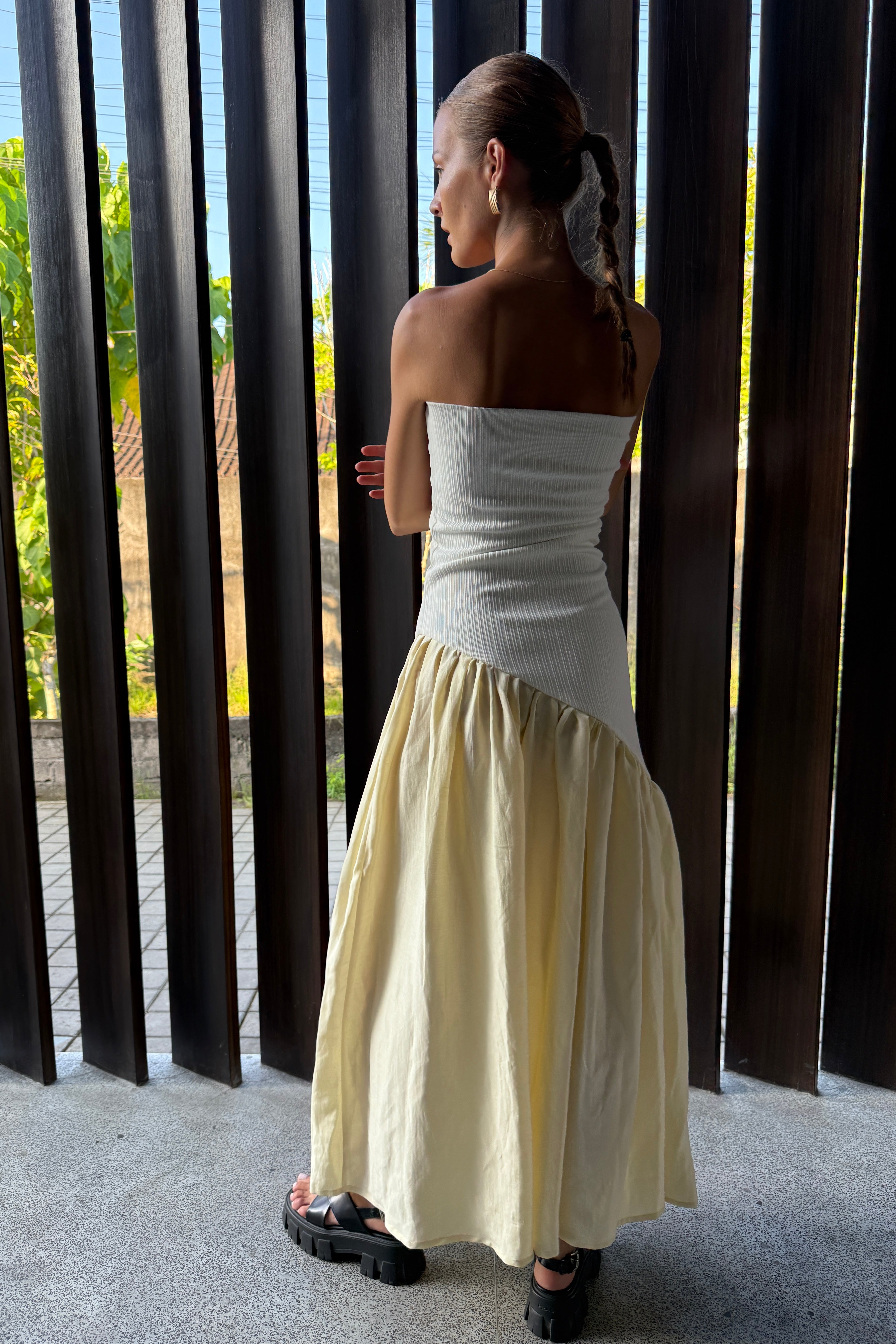 Woman in strapless white maxi dress with asymmetric artfully gathered lemon skirt. Top flatters the figure and skirt adds flow with every movement. Perfect for beach outings and summer soirées.