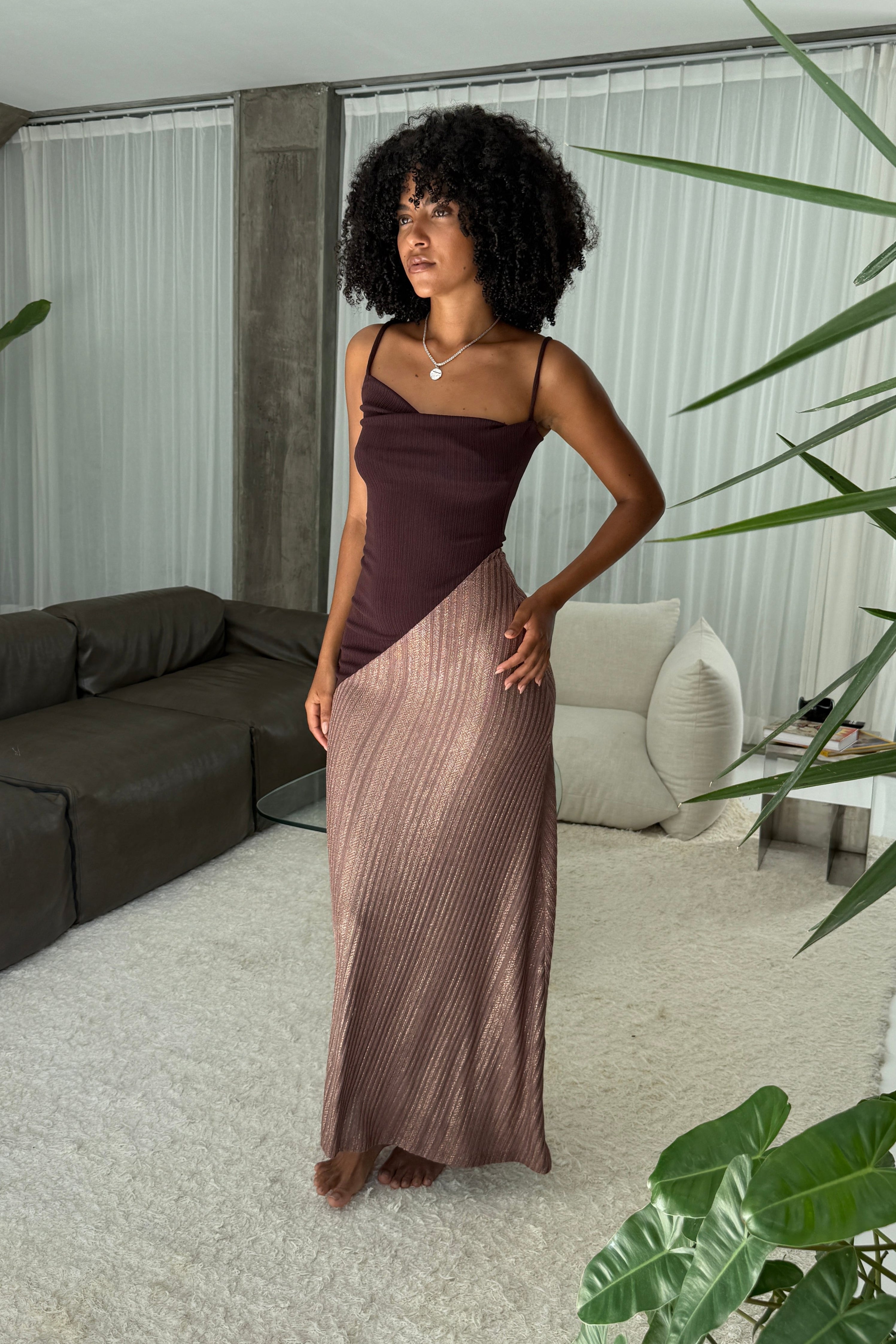 Woman in a long brown dress with cowl neck and asymmetric sparkly toffee skirt. Spaghetti straps and maxi length. Styled with silver necklace.