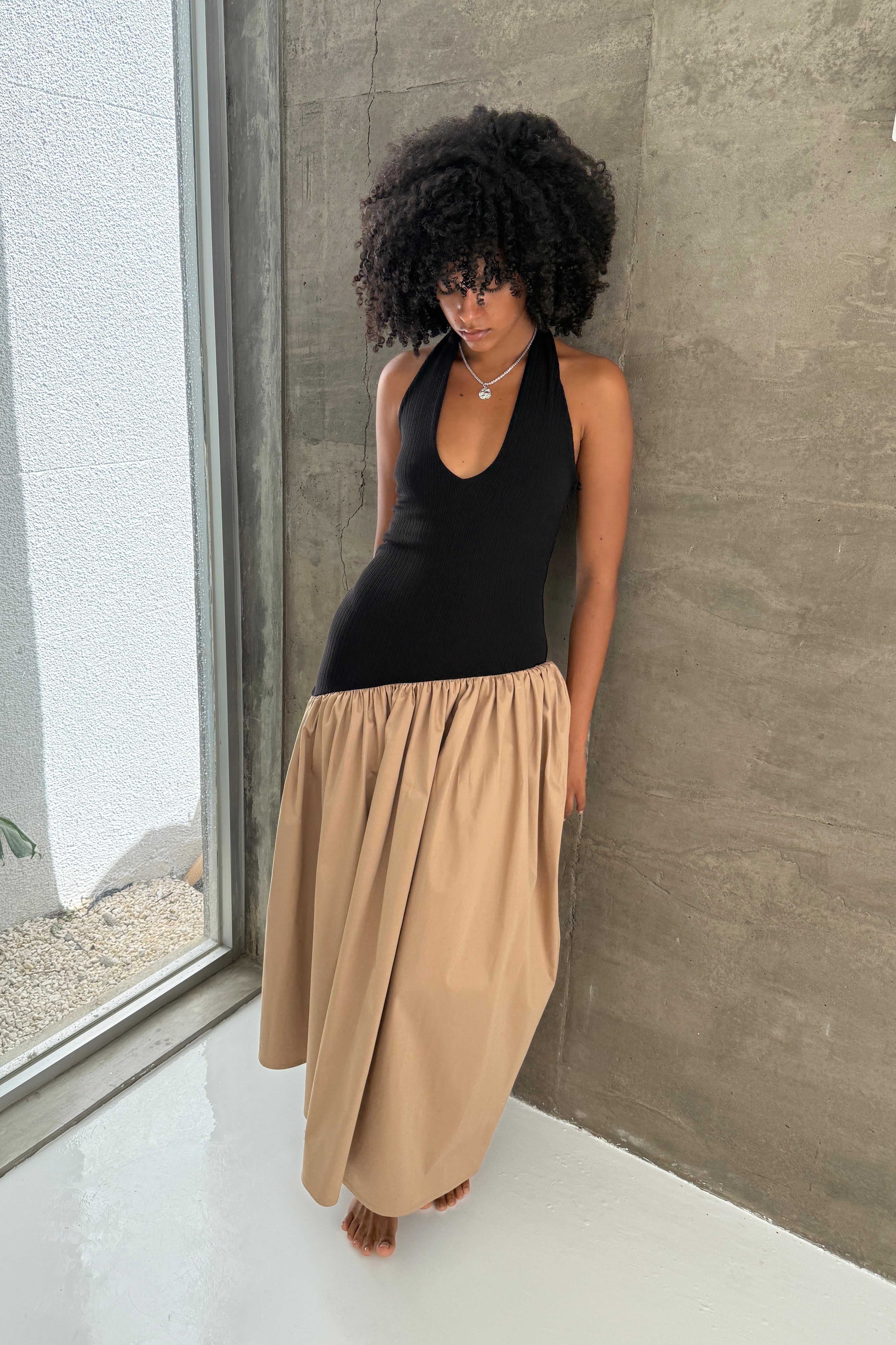 Black halter maxi dress with v-neck line and asymmetric artfully gathered beige skirt. Top flatters the figure and skirt adds flow with every movement. Perfect for beach outings and summer soirées. Styled with a silver necklace