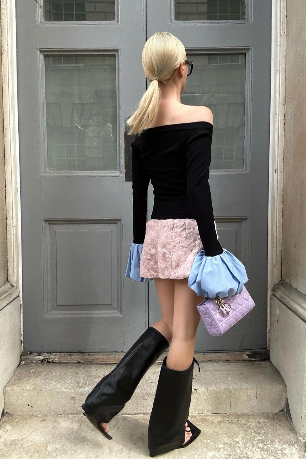 Woman in black long sleeve rib knit top with round neckline and blue balloon details on cuffs. Styled off the shoulder with a pink fur mini skirt.