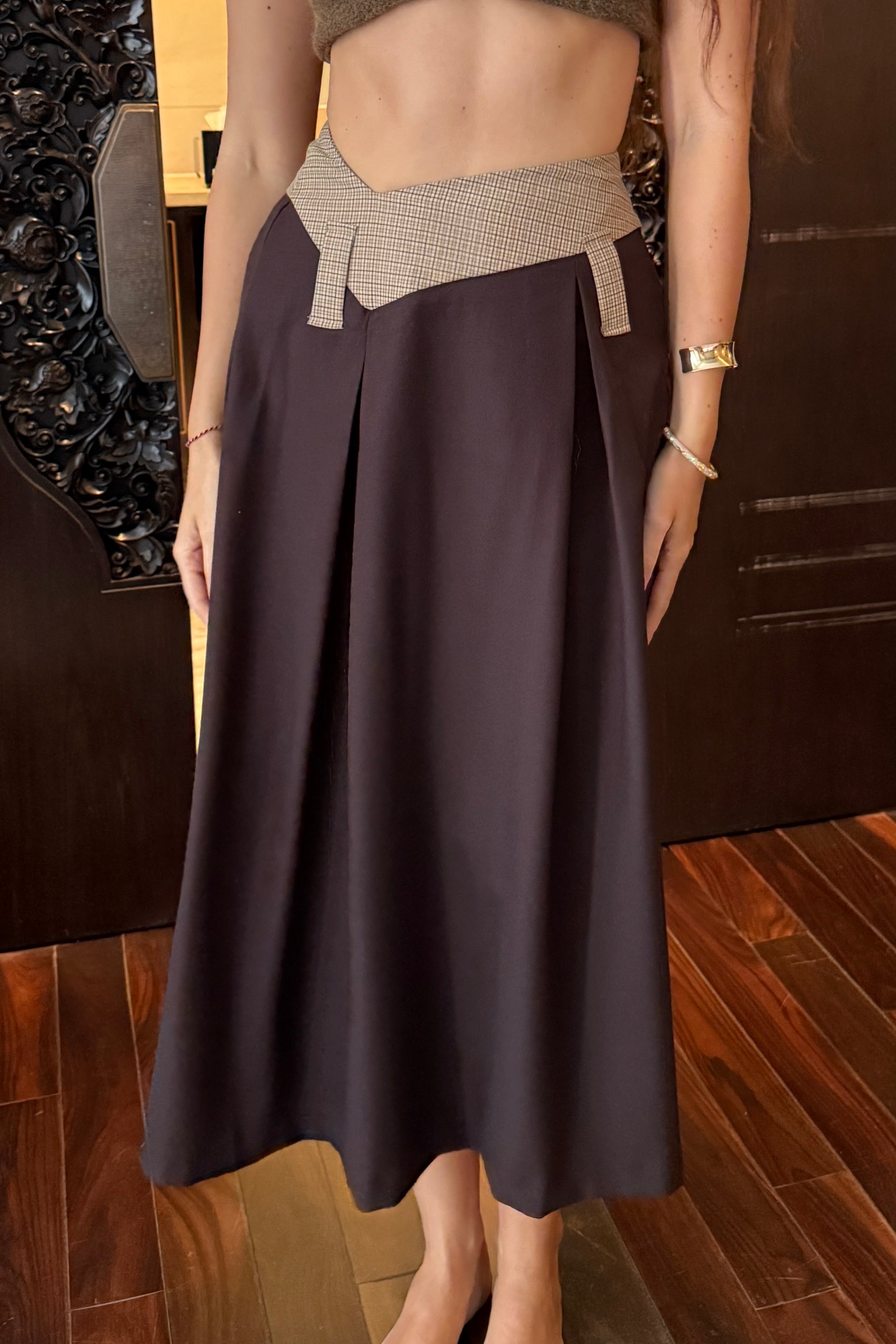 Woman in long skirt with box pleats and dipped waistband. Brown and beige check colourway.