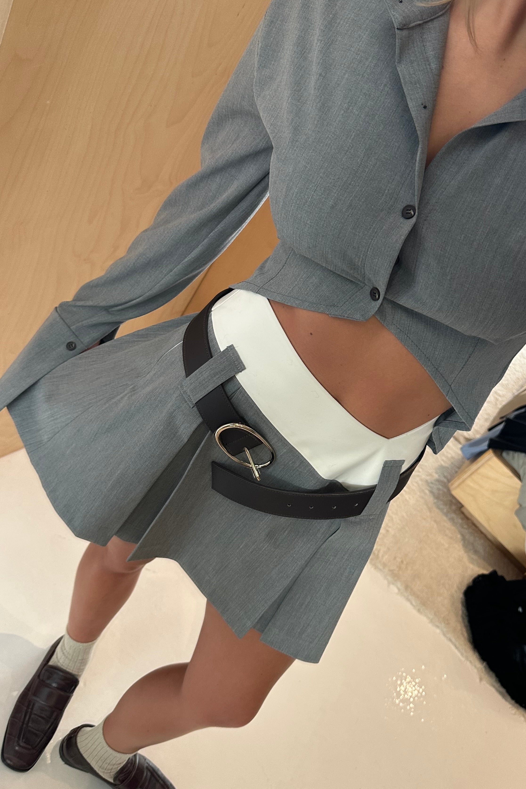 Grey tailored, cropped button down shirt with exaggerated collar and pointed hem. Styled with matching grey mini skirt.