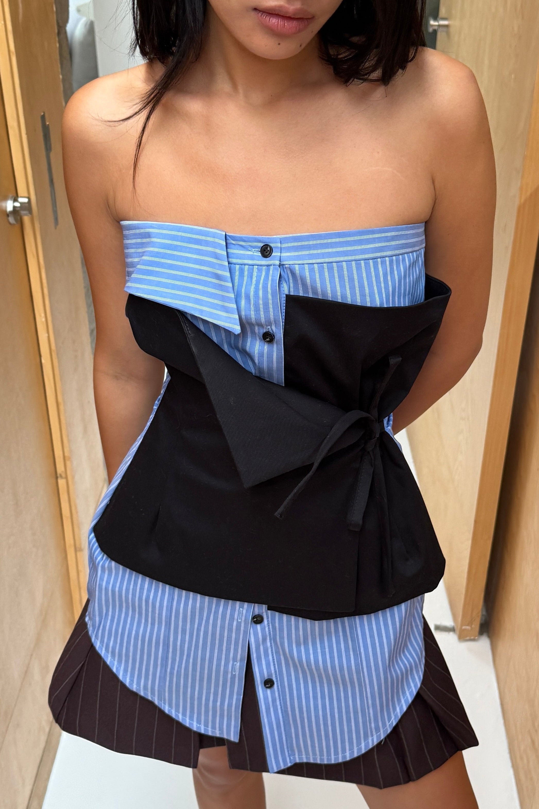 Woman in blue striped strapless top with elements of traditional shirting. Layered black asymmetric tie front detail.