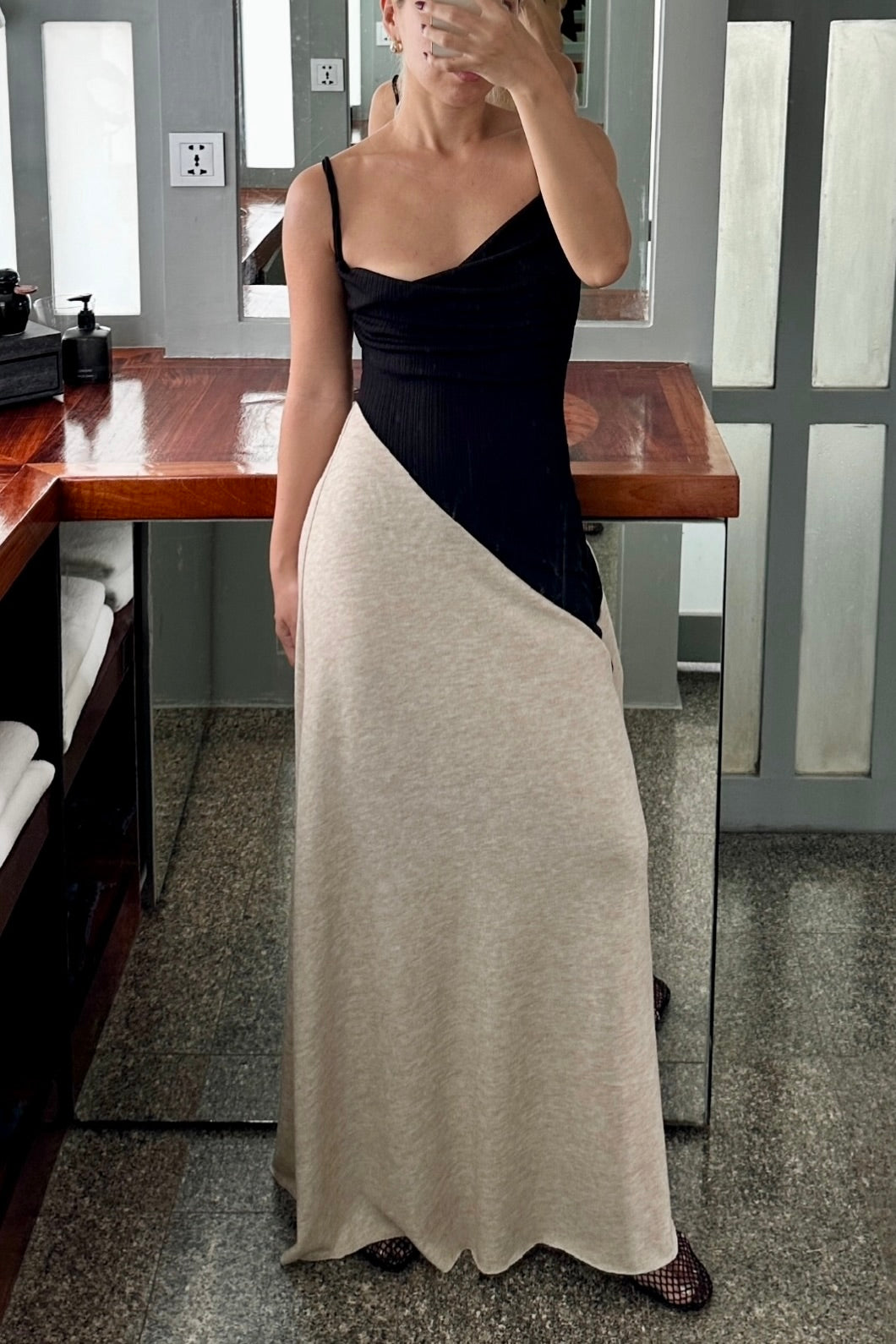 Woman in a long black dress with cowl neck and asymmetric beige skirt. Spaghetti straps and maxi length. Summer soirée essential.