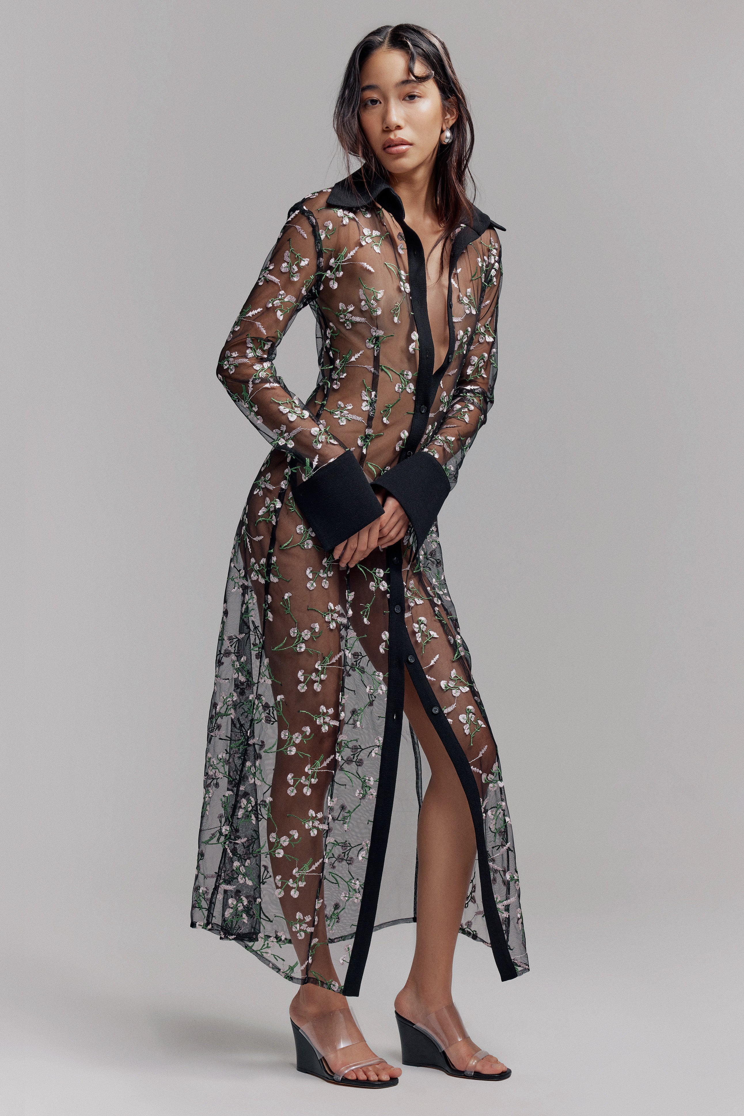 Woman in black maxi sheer shirt dress with opaque black collar and cuffs. Pink and green floral details on fabric, perfect for Summer.