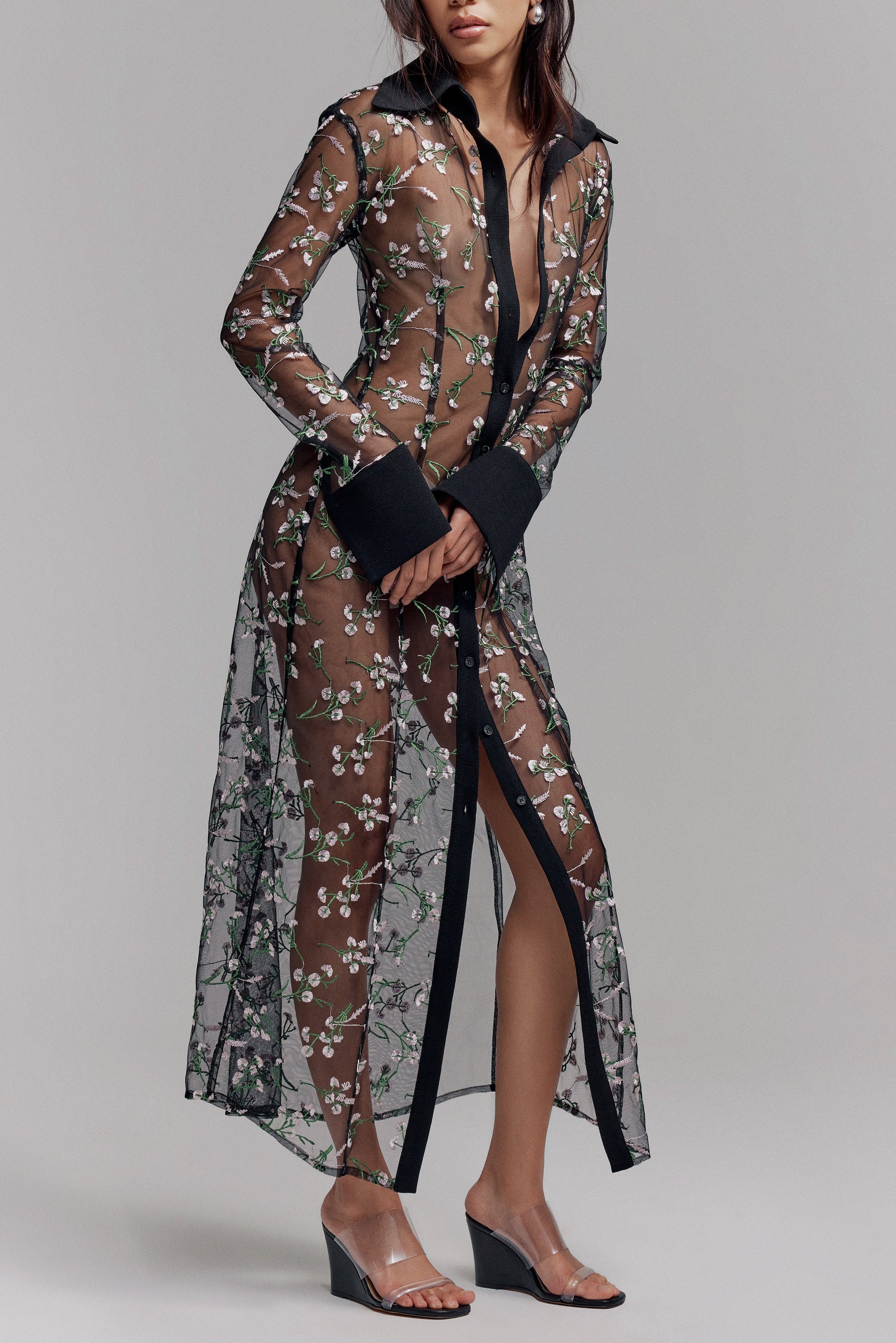 Woman in black maxi sheer shirt dress with opaque black collar and cuffs. Pink and green floral details on fabric, perfect for Summer.