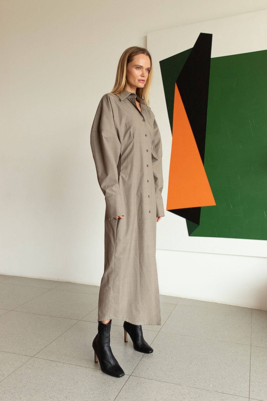 Woman in a long beige coat standing in front of a colorful abstract painting.