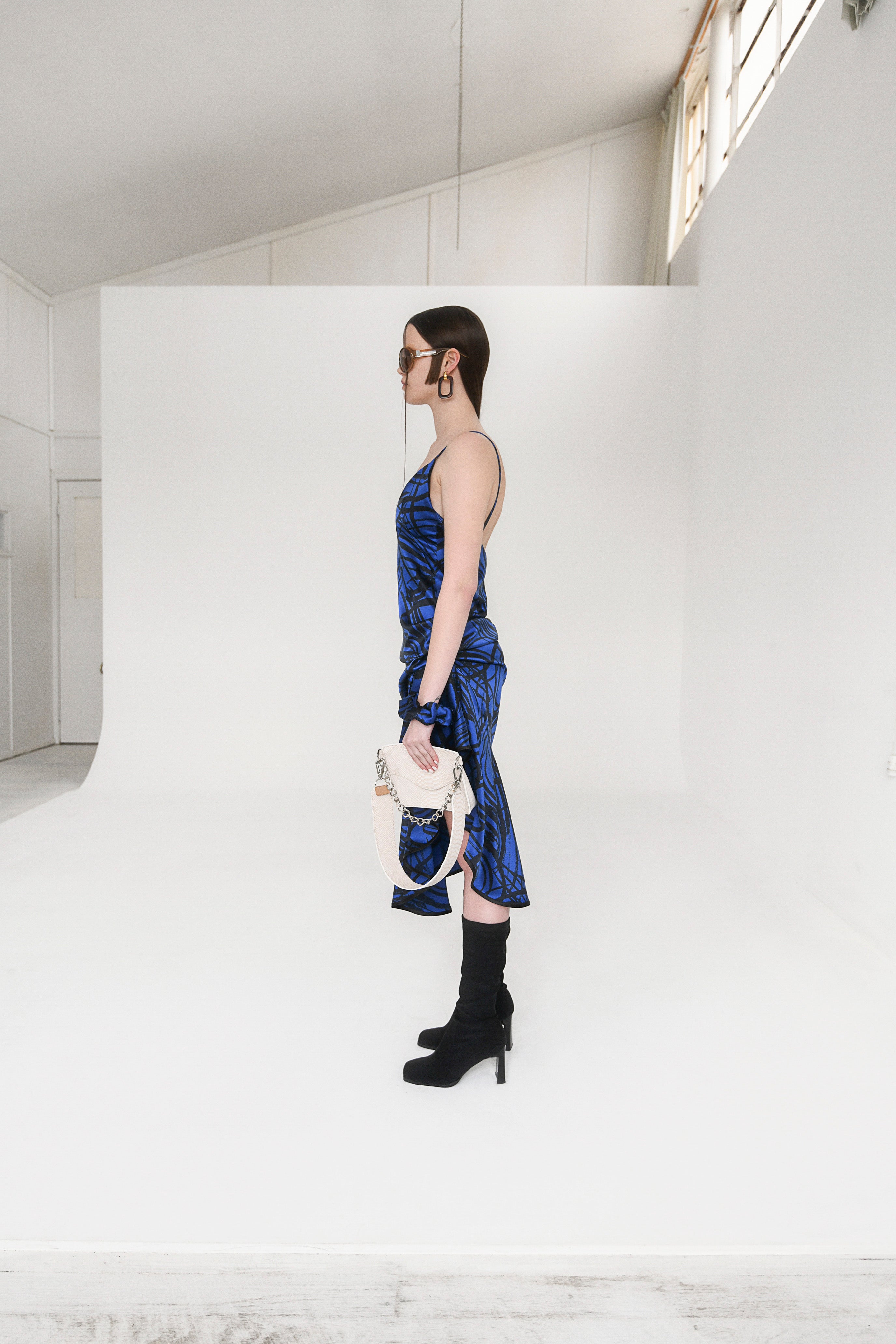 Woman in flouncy dress with black and royal blue spiral pattern. Midi length, spaghetti straps, ruffles in the skirt, v-neck, low back, asymmetric hem. Perfect for Summer.