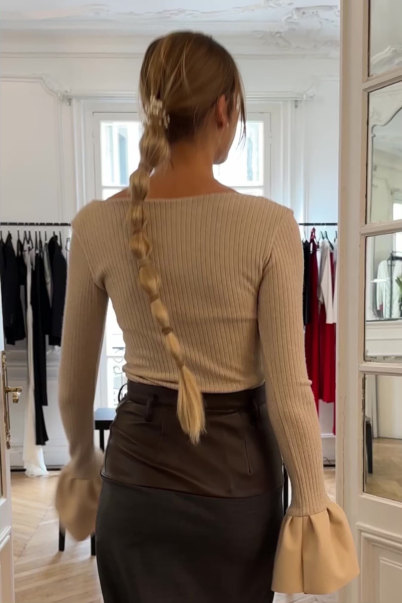 Woman in beige soft rib knit top with v-neck, long sleeves, and flared cuff details. Styled with black maxi skirt.