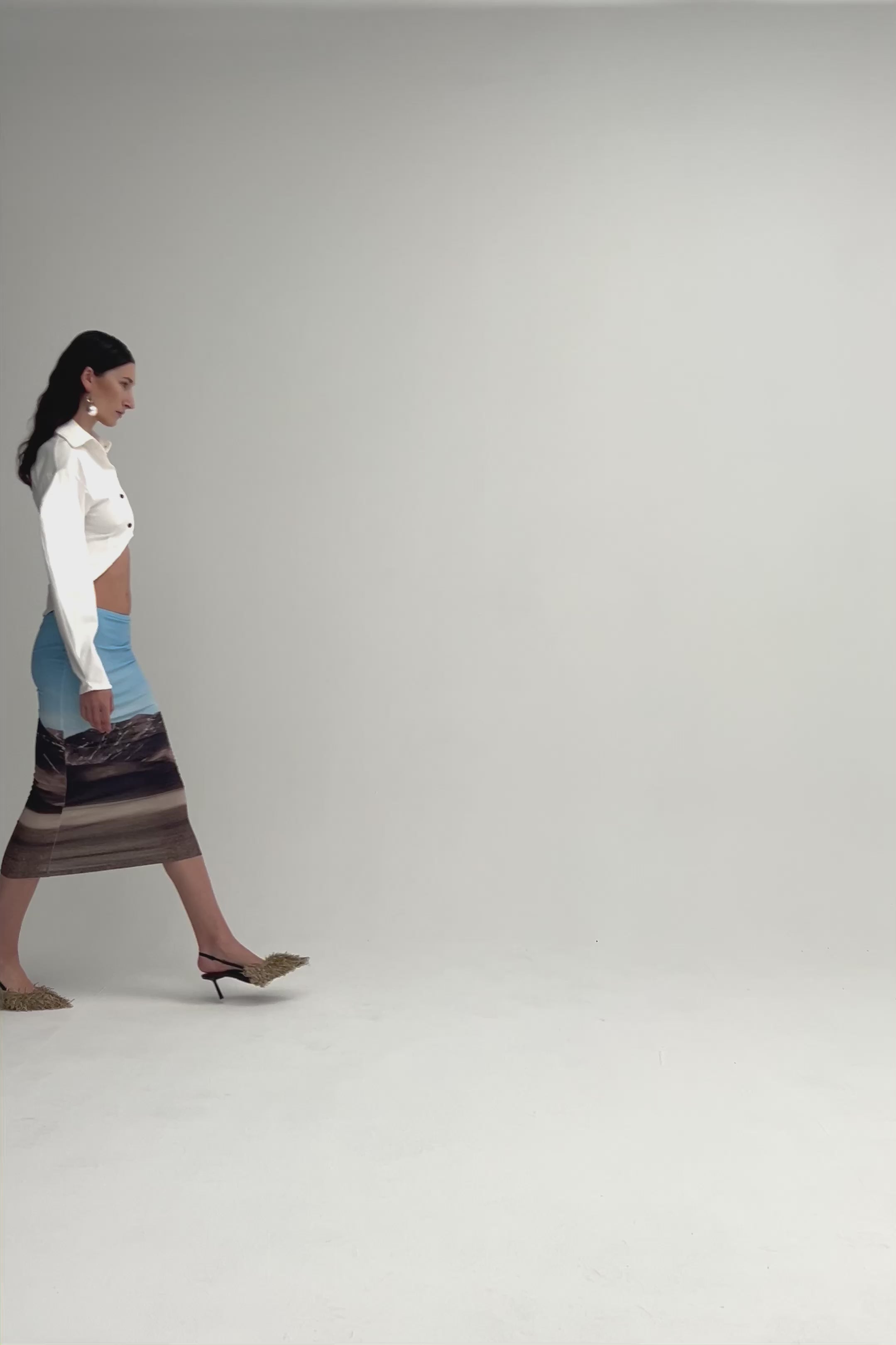 Woman in volume sleeve white button up shirt with cornered hem. Styled with a landscape print pencil skirt.