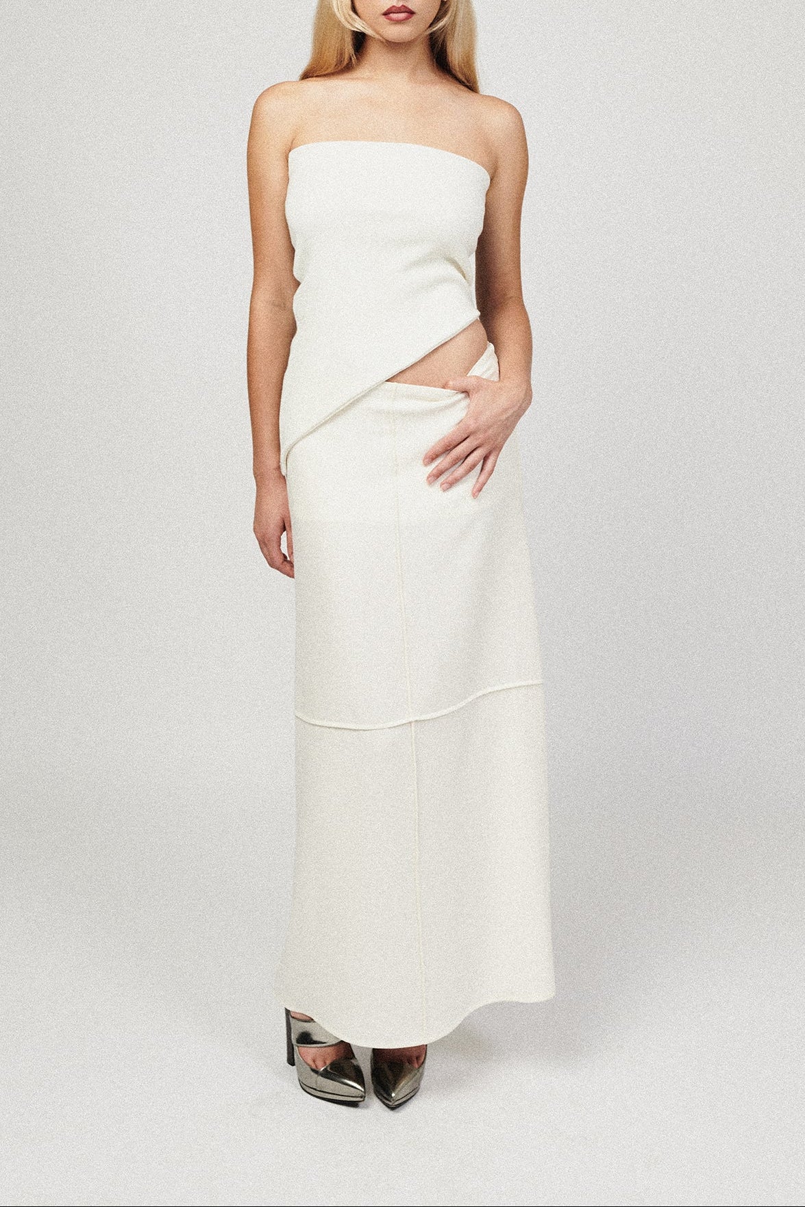 Woman in white long skirt with grid pin tuck detail. Paired with white sleeveless top.