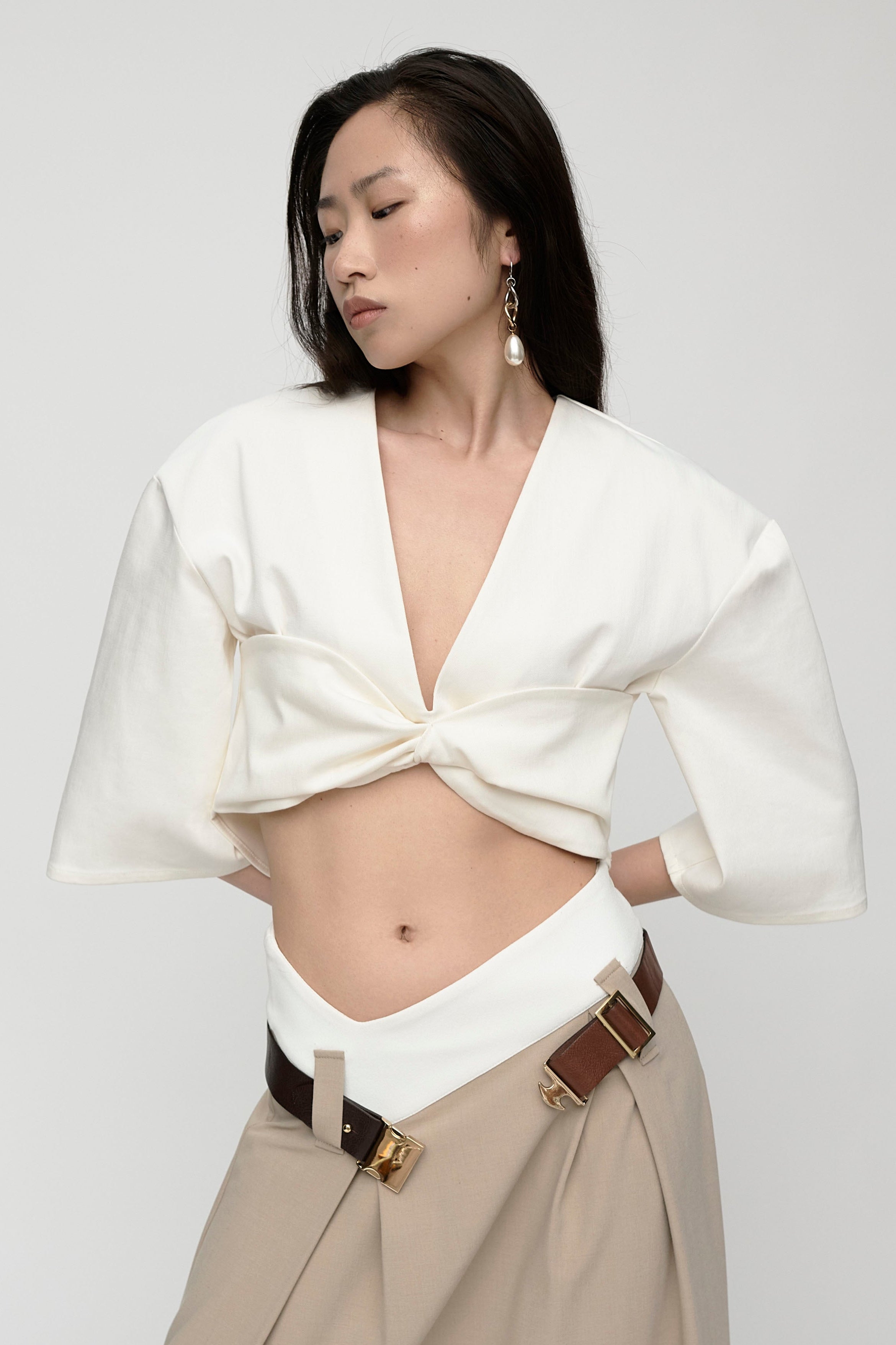 Woman in mid length sleeve, v-neck, cropped white top. Styled with long beige skirt and boots.