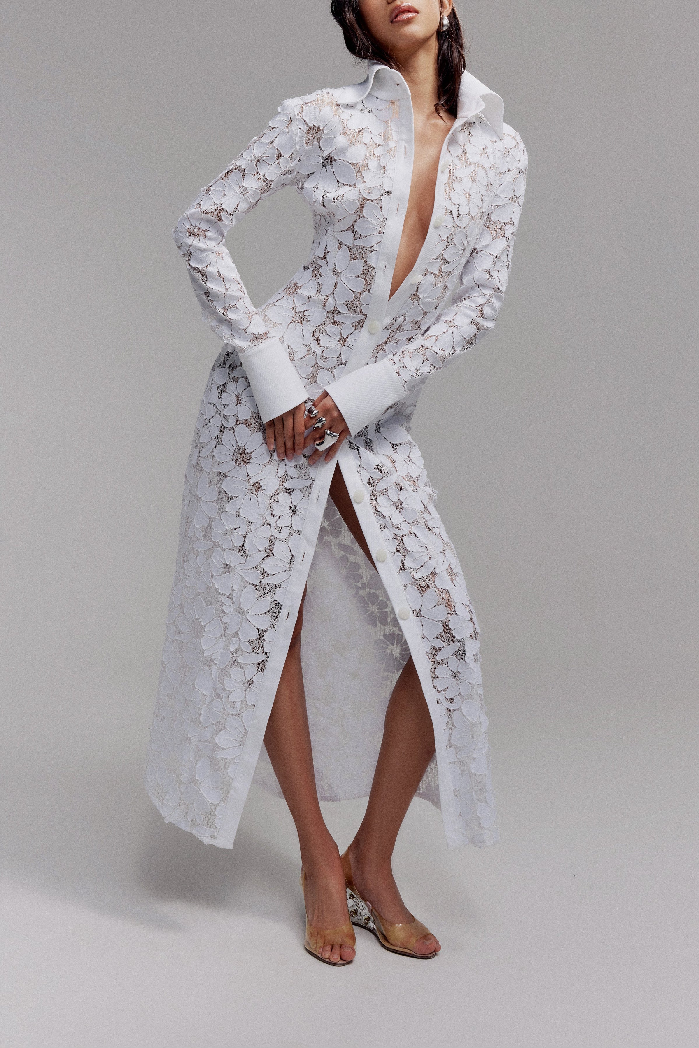 Woman in maxi white lace shirt dress with long sleeves, exaggerated collar and button front closure.