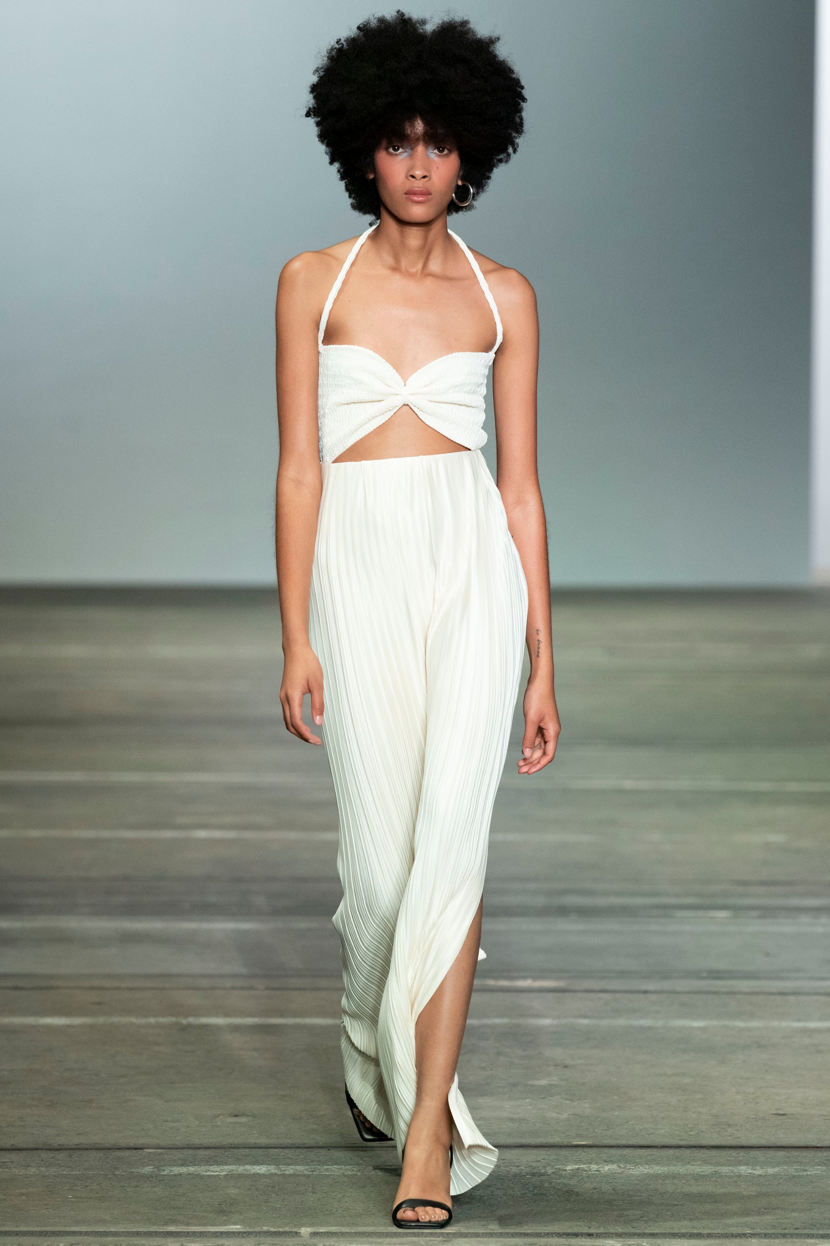 Woman in white halter neck maxi dress. Featuring side slits and soft pleating in the skirt and cut out and cinched bust detail on the top. Perfect for vacation.