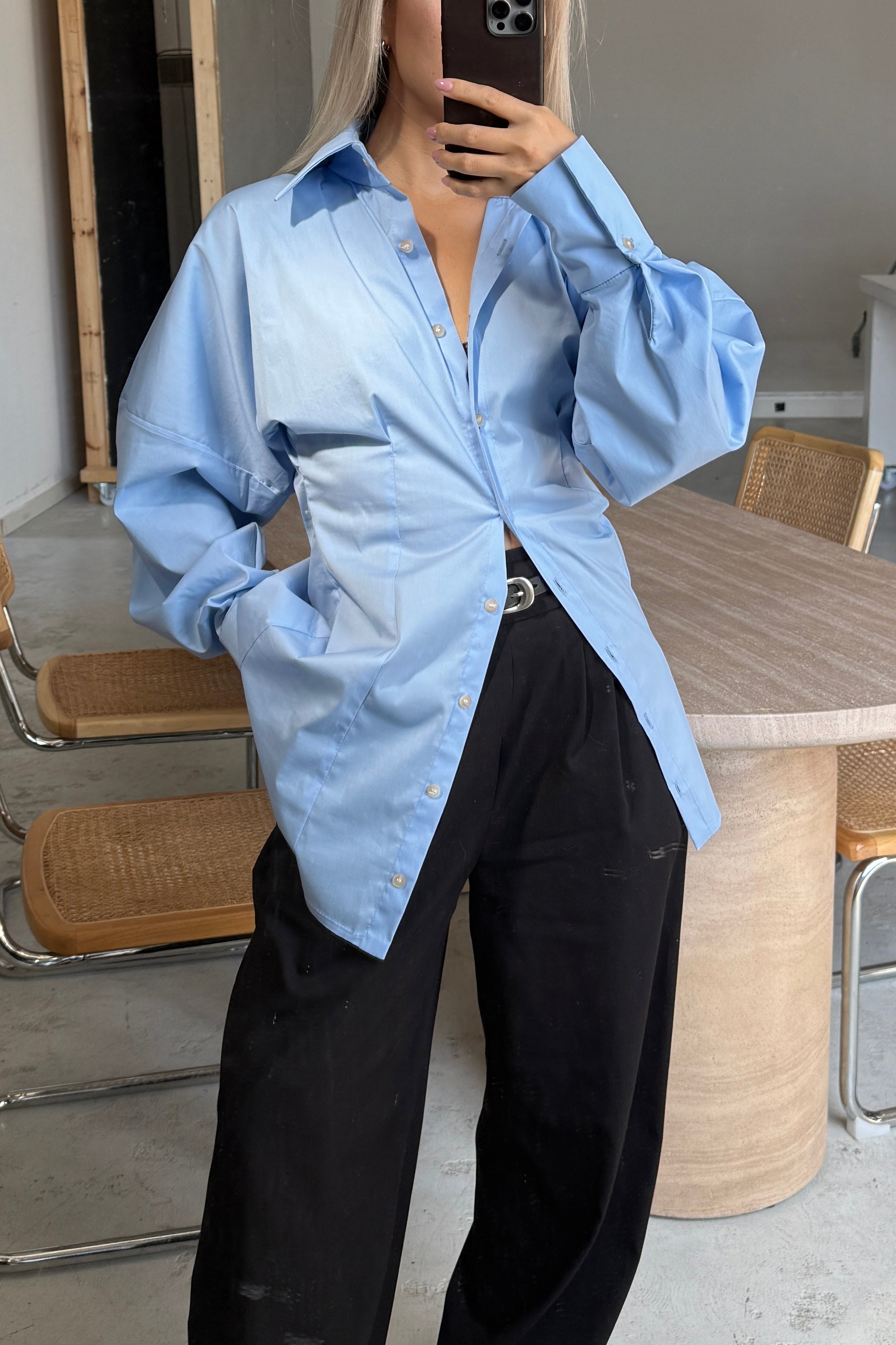 Woman in baby blue volume sleeve shirt dress. Slightly unbuttoned and styled over black trousers.